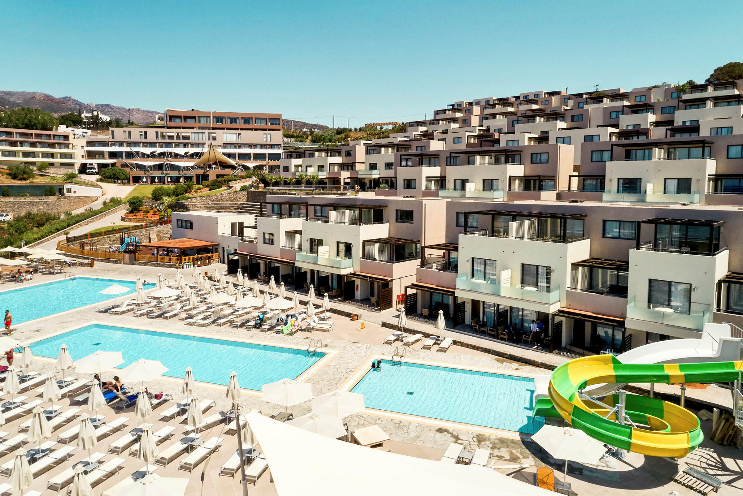 Hotellområde med pooler, solstolar och vattenrutschkana framför byggnader. (AI-genererad text)
