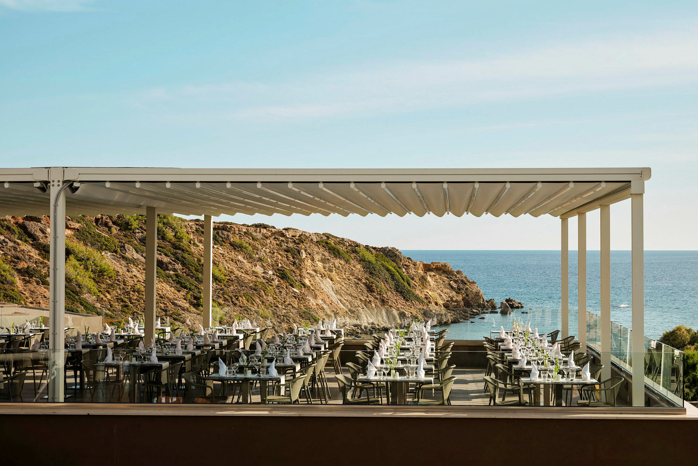 En utomhusrestaurang med dukade bord och utsikt över havet och klippor. (AI-genererad text)
