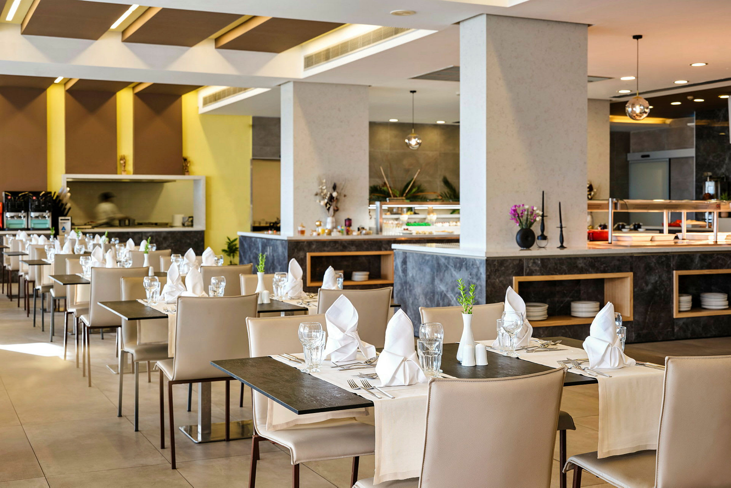En modern restaurang med dukade bord, beige stolar och servetter placerade på varje bord. (AI-genererad text)