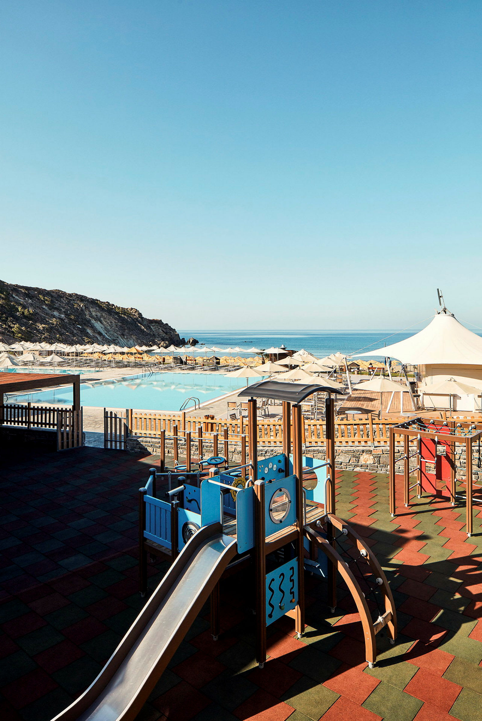 Lekplats med rutschkana nära en pool och solstolar med utsikt över havet. (AI-genererad text)
