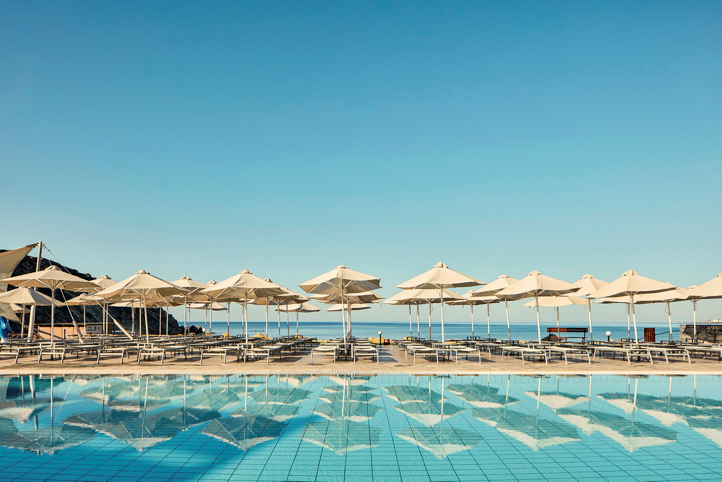 Solstolar och parasoller vid en swimmingpool med havet i bakgrunden. (AI-genererad text)