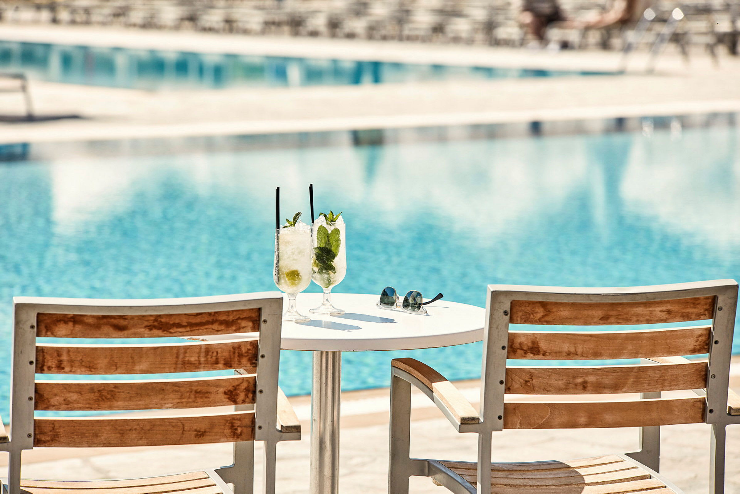 Två solstolar och ett bord med två glas med drinkar vid en pool. (AI-genererad text)