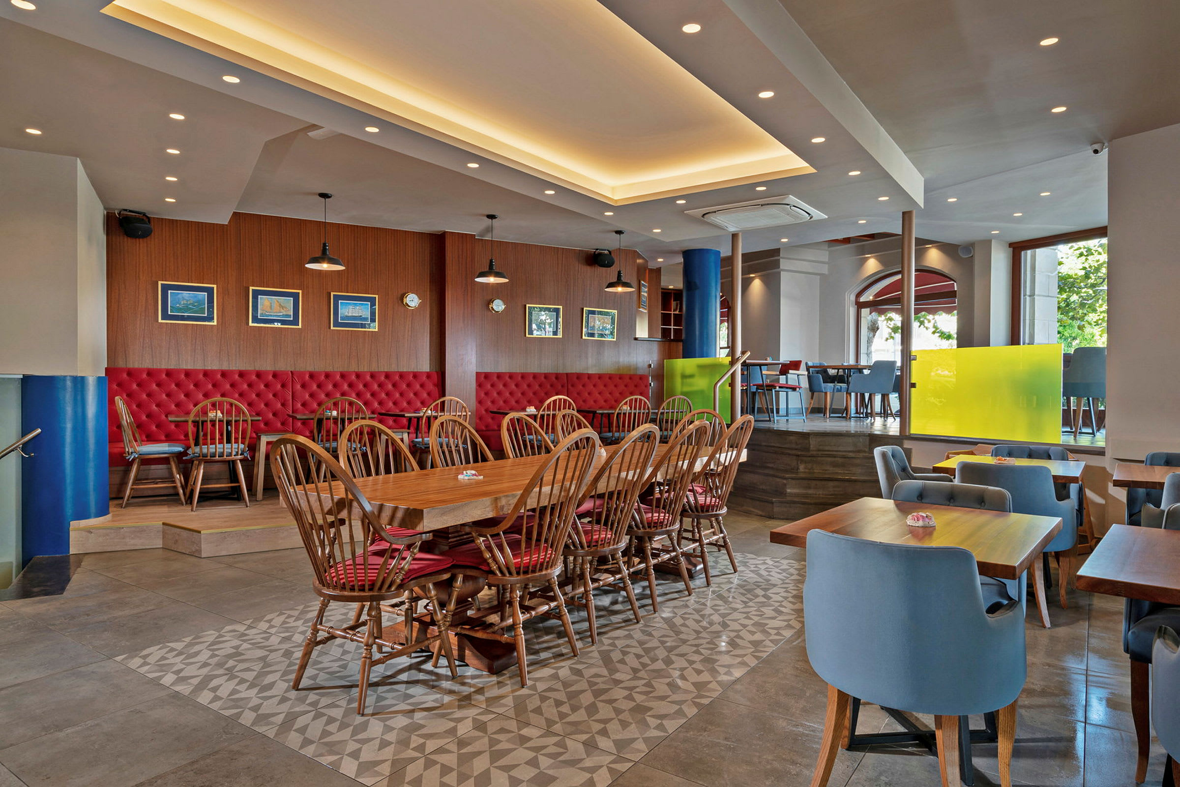 En restaurang med möbler som inkluderar trästolar med röda dynor och bord placerade på ett kaklat golv. (AI-genererad text)