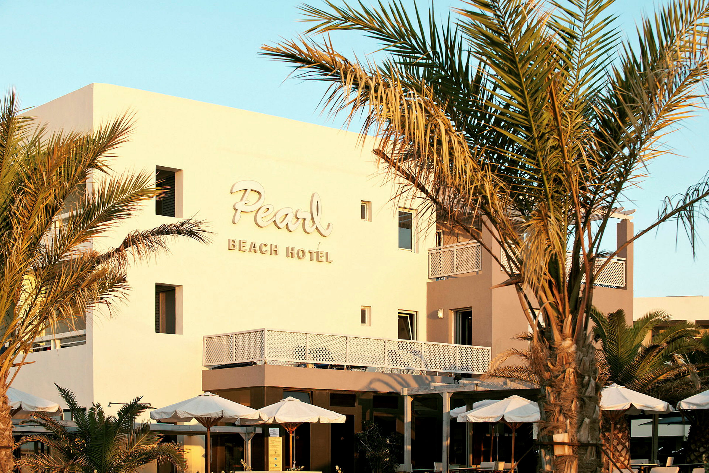 Fasad av Pearl Beach Hotel med omgivande palmer och parasoller. (AI-genererad text)