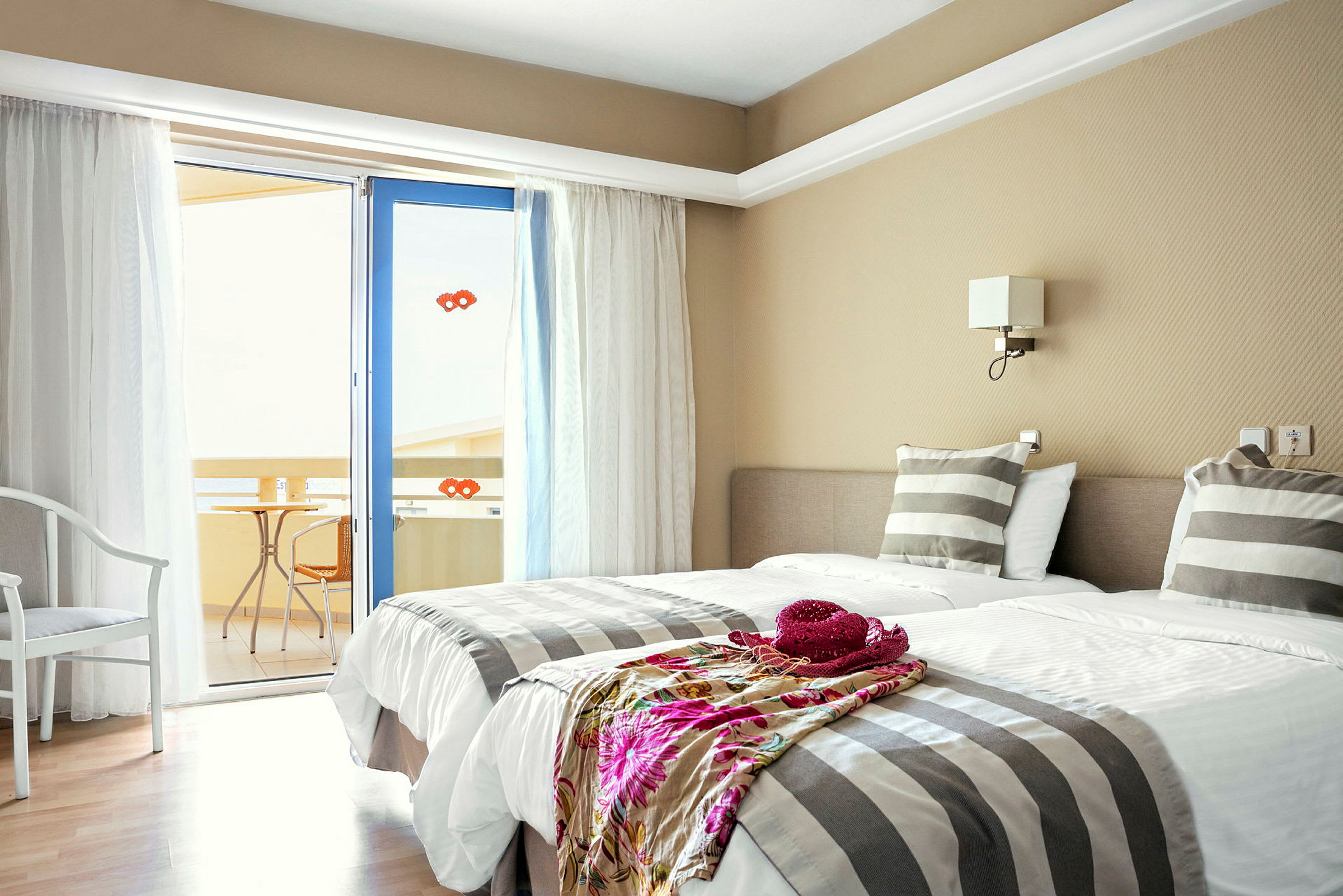 Ett hotellrum med två enkelsängar, randiga sängkläder och en dörr till en balkong. (AI-genererad text)