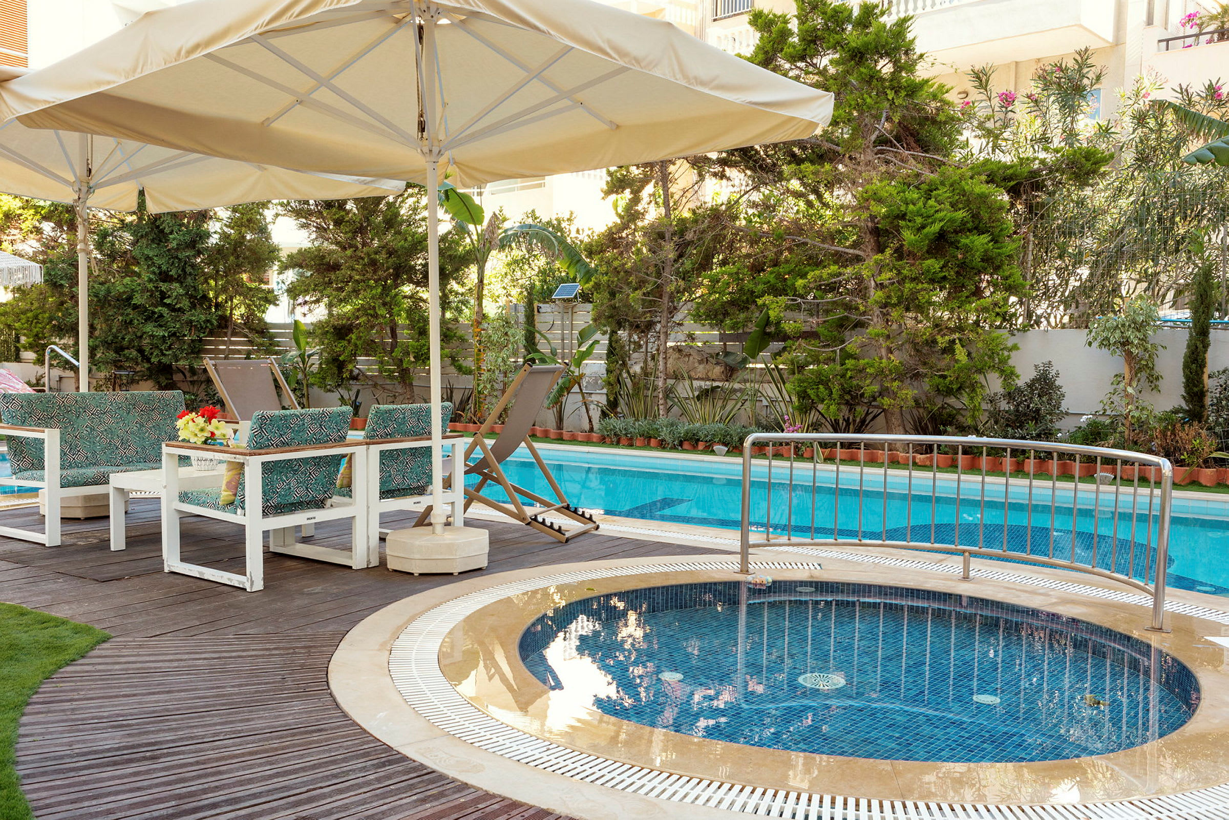 Ett poolområde med parasoller, solstolar och sittmöbler vid en swimmingpool och en mindre jacuzzi. (AI-genererad text)