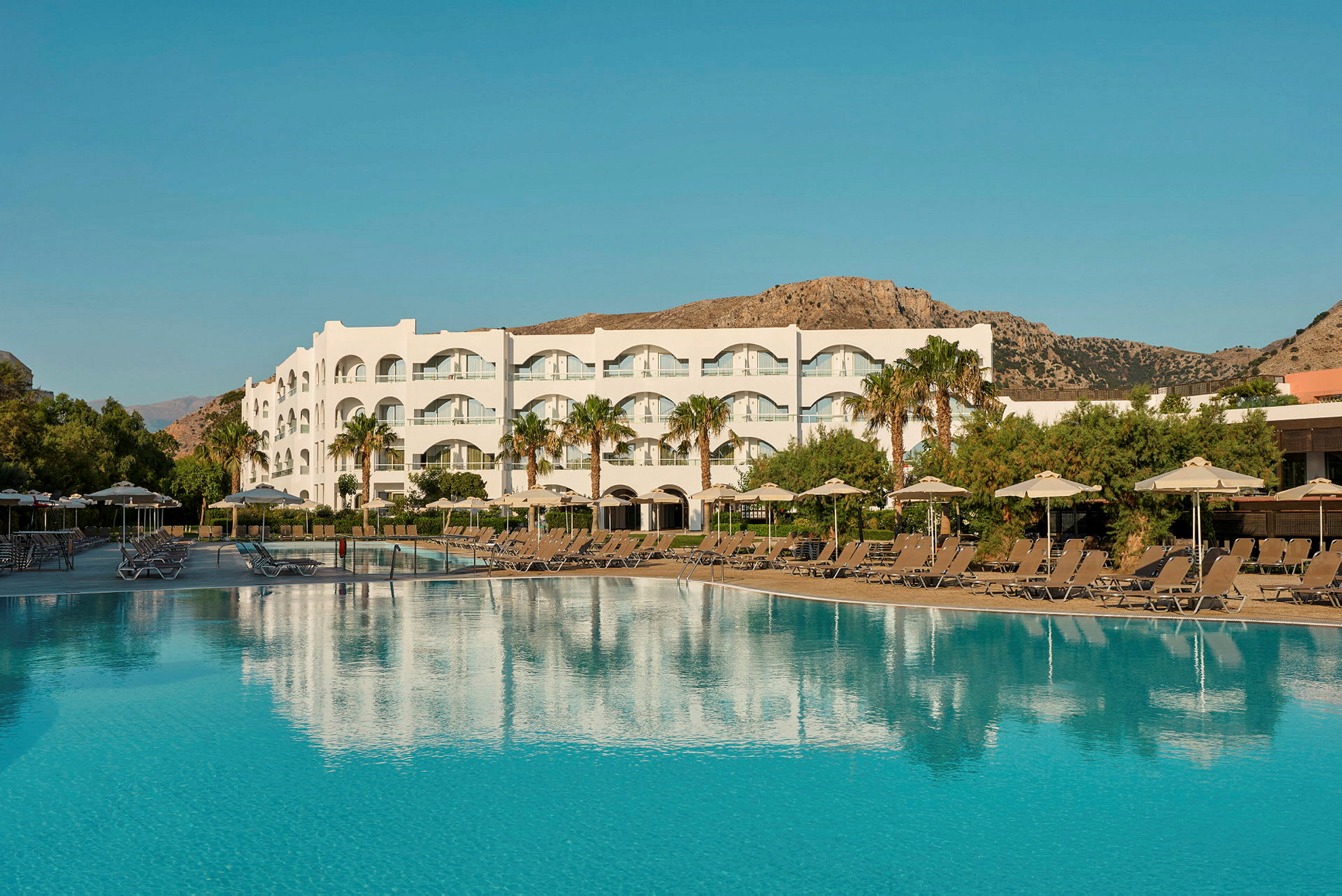 En stor pool framför en vit hotellbyggnad med balkonger. (AI-genererad text)