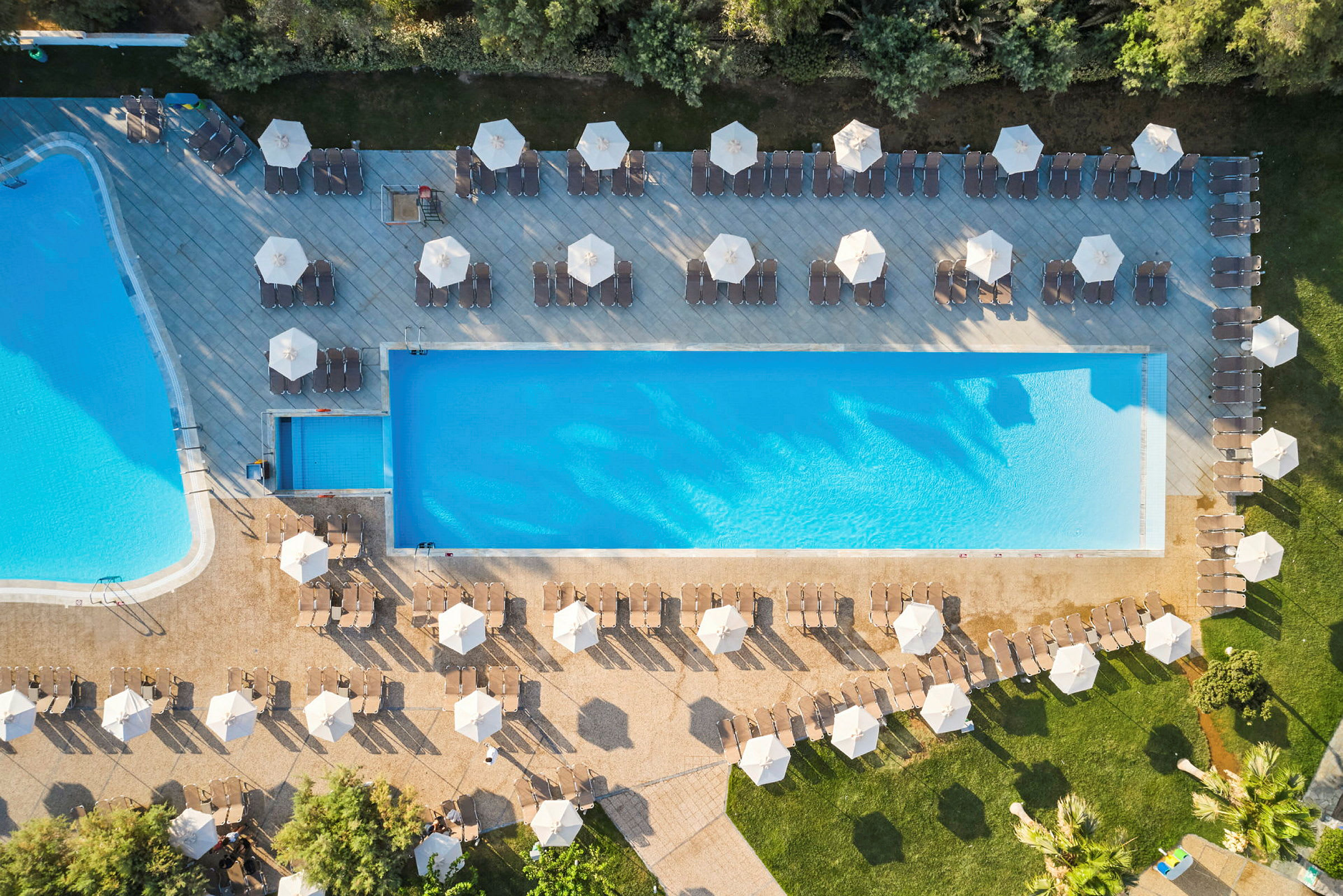 Flygfoto av en pool med solstolar och paraplyer runtom. (AI-genererad text)