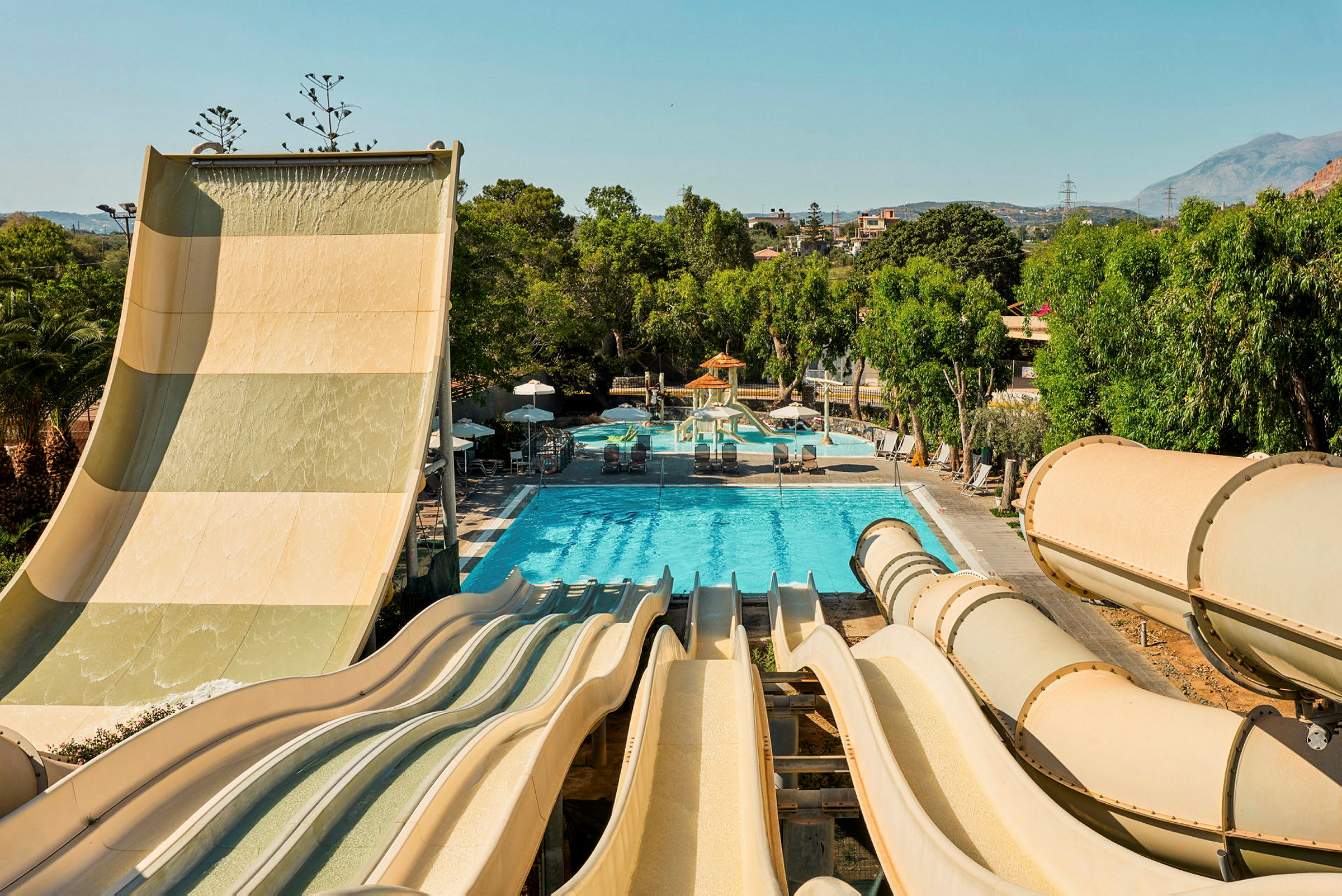 Bild av en vattenpark med flera vattenrutschbanor som leder ner till en pool omgiven av gröna träd. (AI-genererad text)