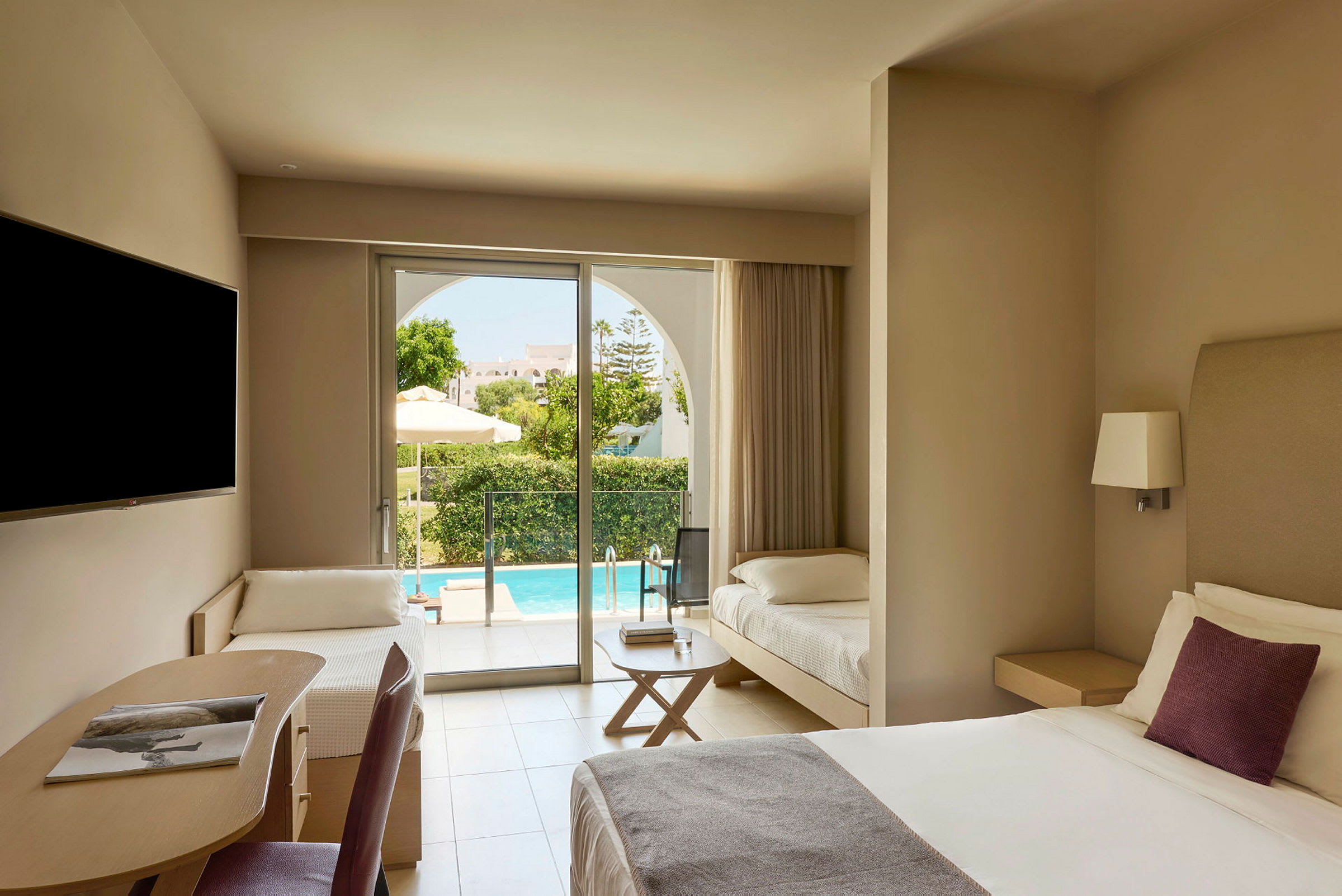 Ett hotellrum med en dubbelsäng, en skrivhörna, och en extra säng. Utanför syns en terrass och en pool. (AI-genererad text)