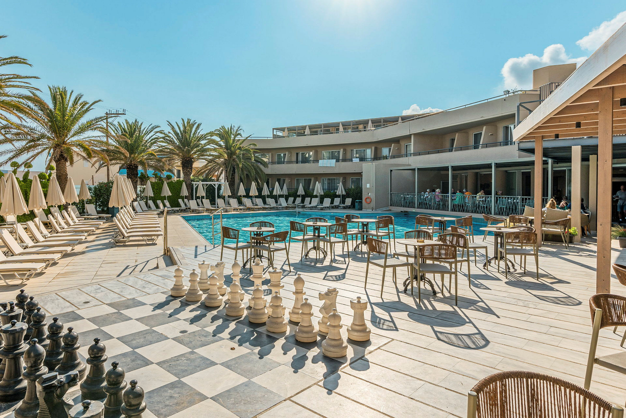 Bild av ett hotellområde med en pool, solstolar, matsal och stort schackspel. (AI-genererad text)