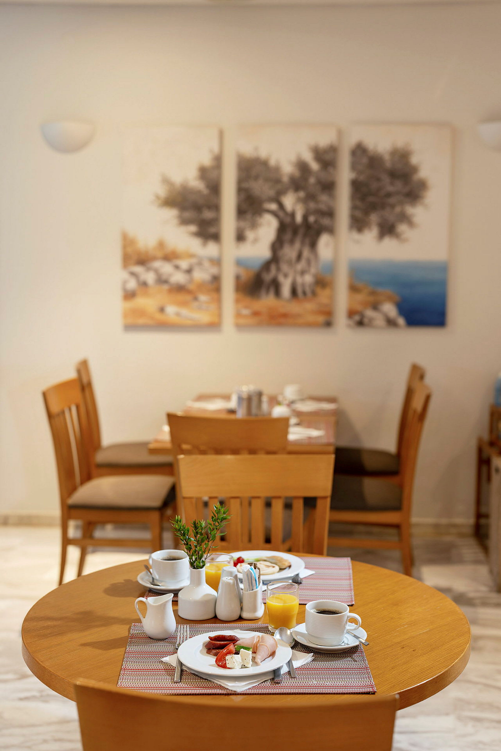 Ett dukat frukostbord med tallrikar, kaffekoppar och juice på en restaurang med trästolar och en väggmålning. (AI-genererad text)