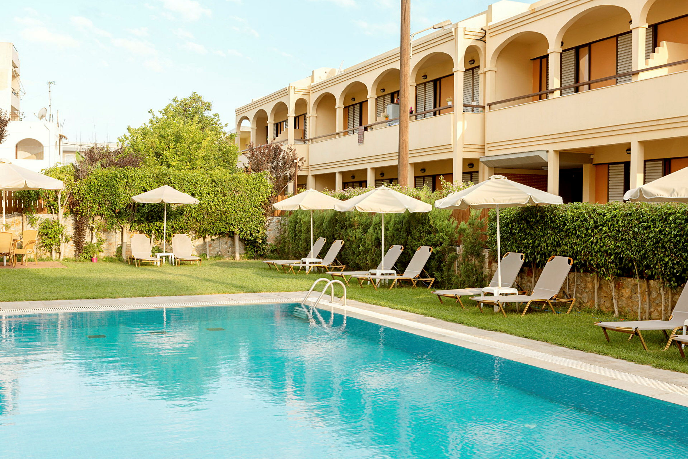 Hotellbyggnad med pool, solstolar och parasoller. (AI-genererad text)