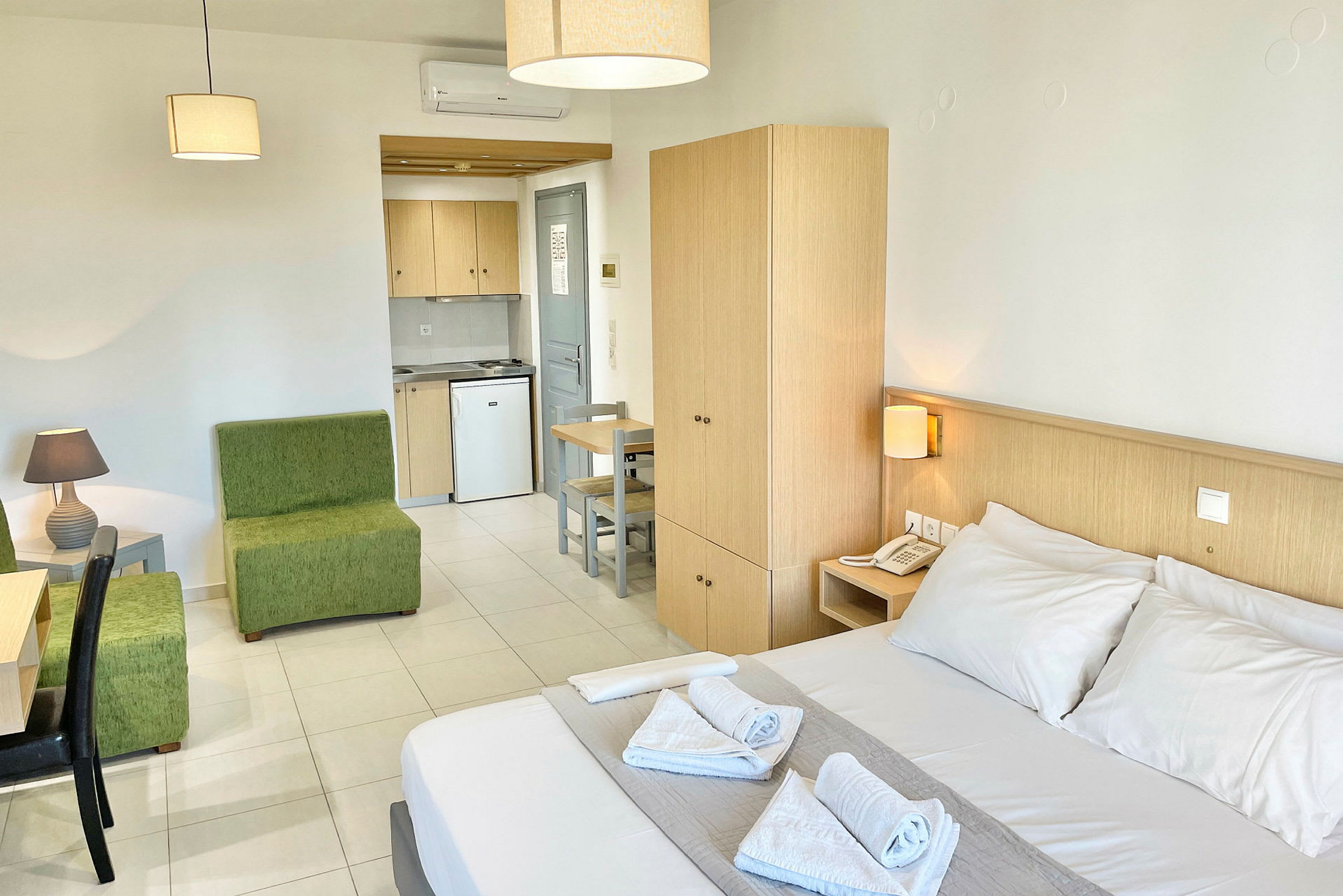 Ett hotellrum med dubbelsäng, grön sittgrupp, skrivbord, garderob och en kokvrå. (AI-genererad text)