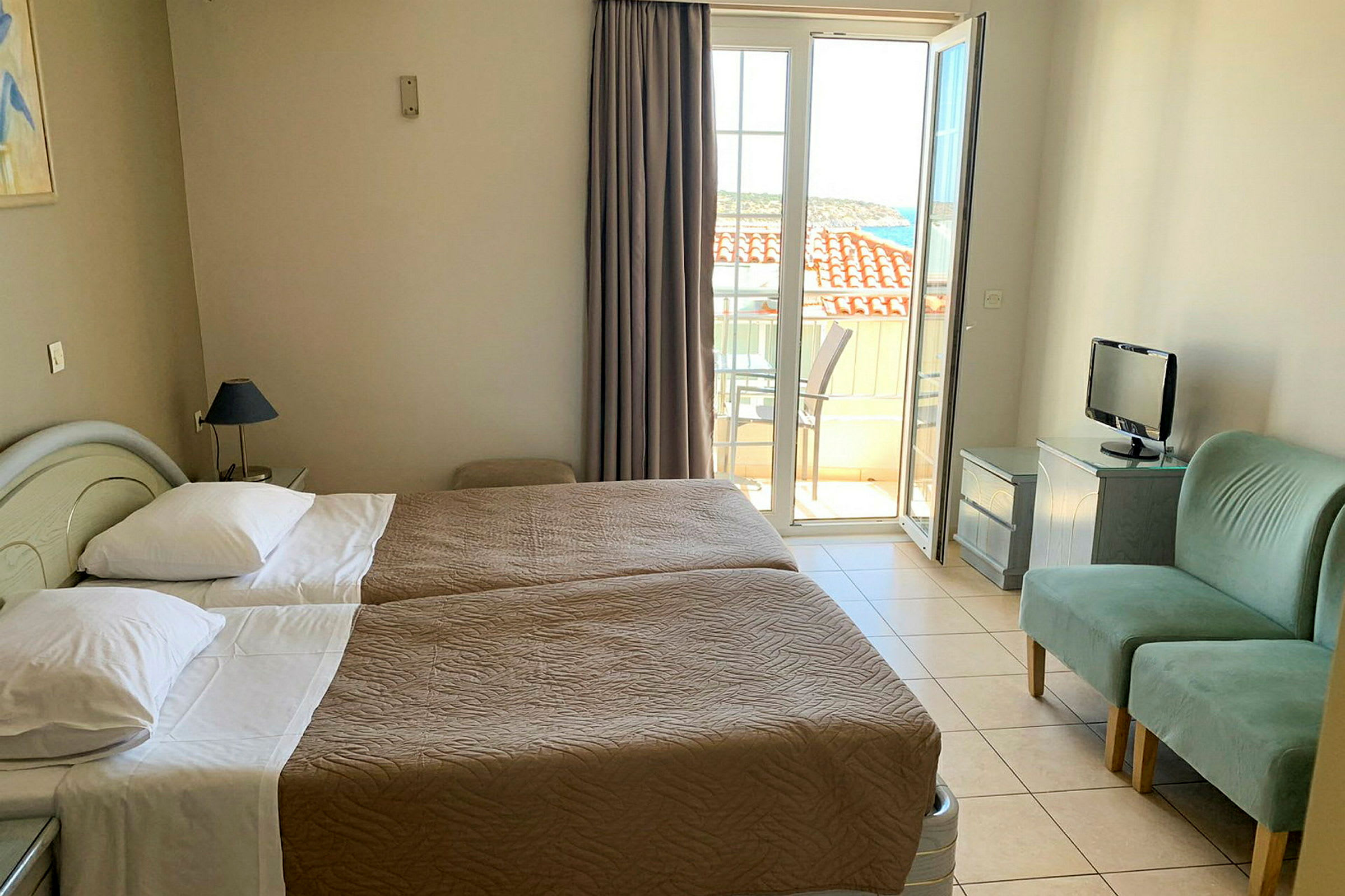 Hotellrum med två enkelsängar, liten TV, två gröna fåtöljer och balkong med utsikt. (AI-genererad text)