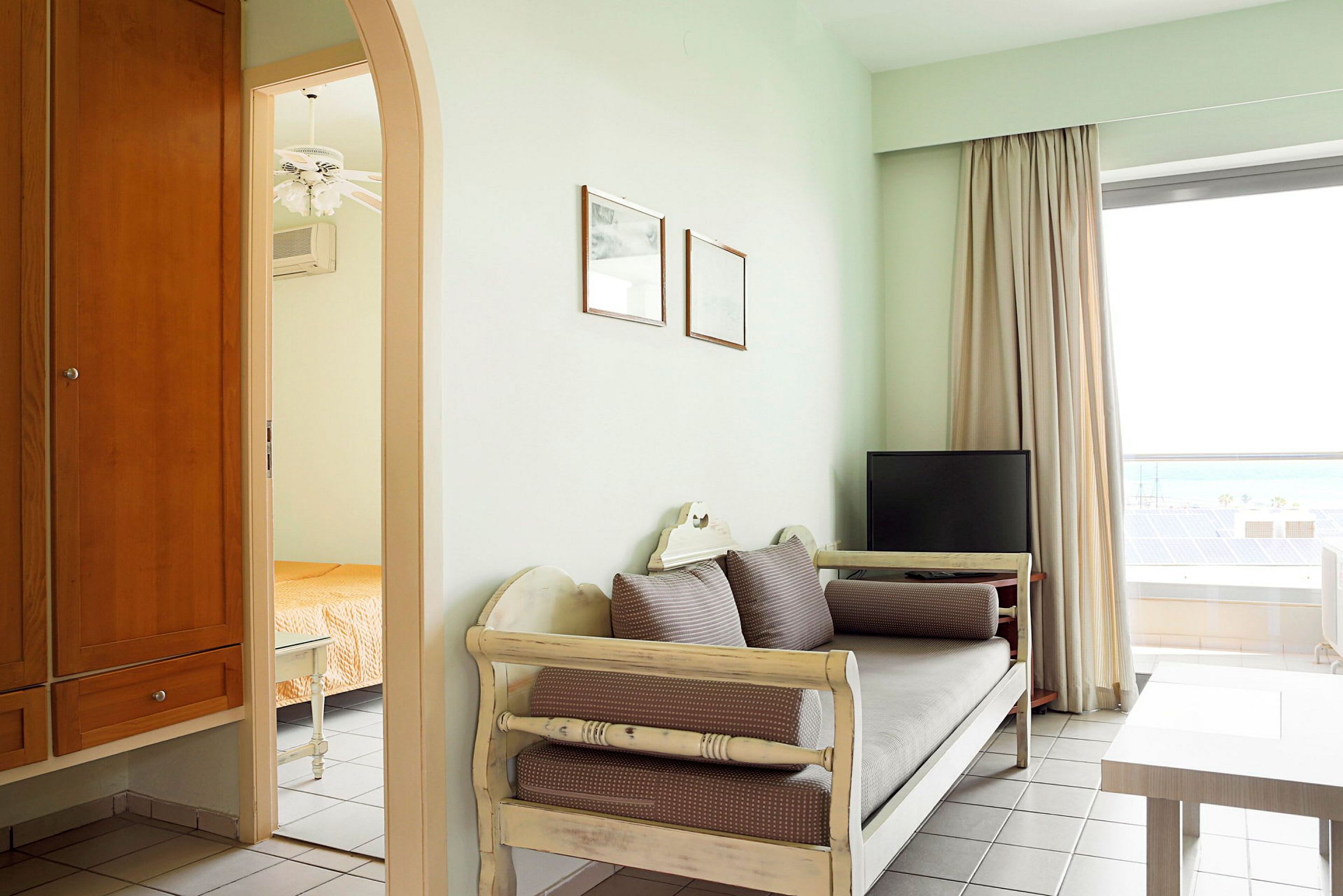 Bild av ett hotellrum med en soffa, ett bord och en TV nära ett fönster, med en öppning mot ett angränsande rum med en säng. (AI-genererad text)