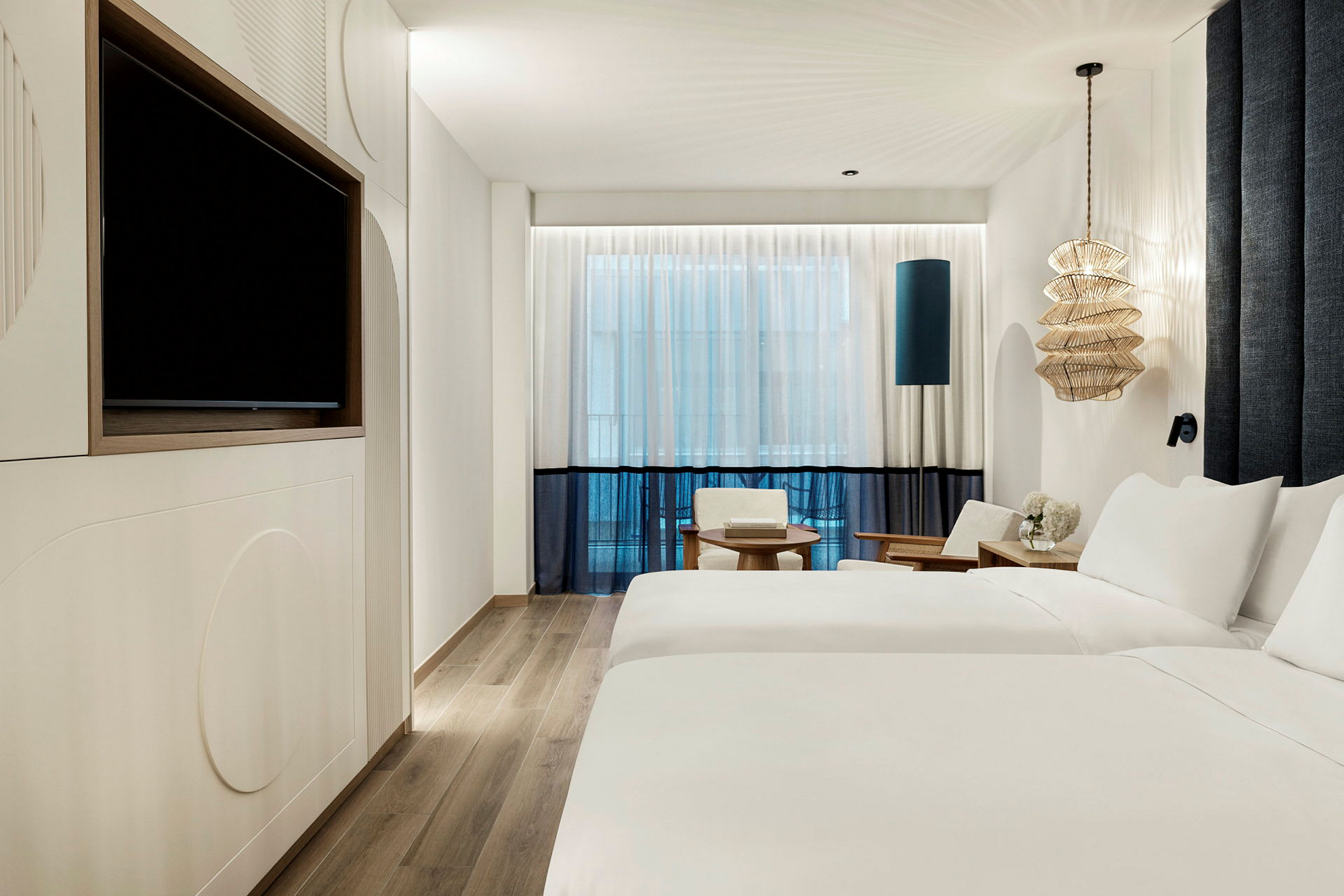 Ett modernt hotellrum med två enkelsängar, en TV på väggen, sittmöbler och en dekorativ lampa. (AI-genererad text)