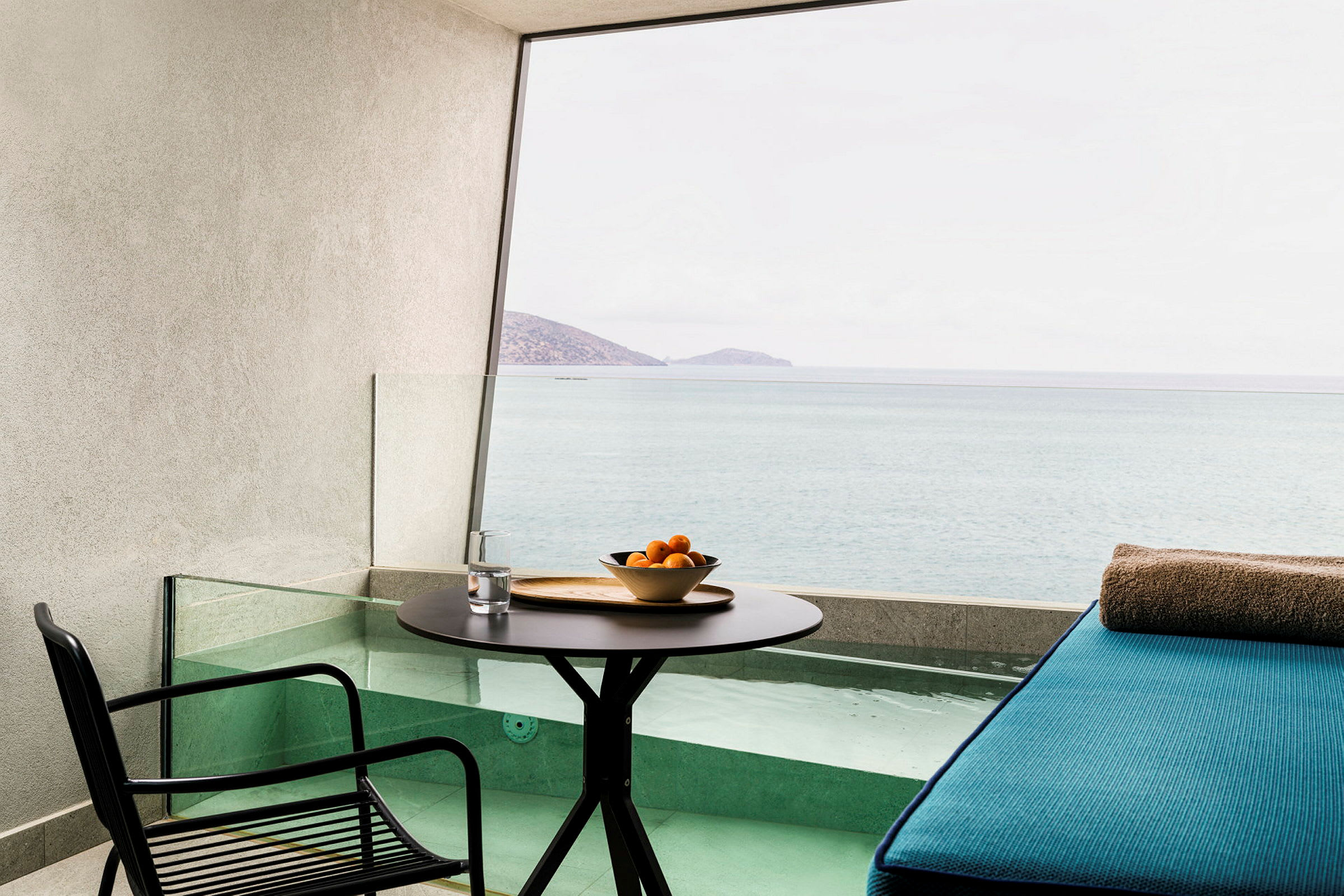 En terrass med bord, stol och en sittplats vid en liten pool med utsikt över havet. (AI-genererad text)
