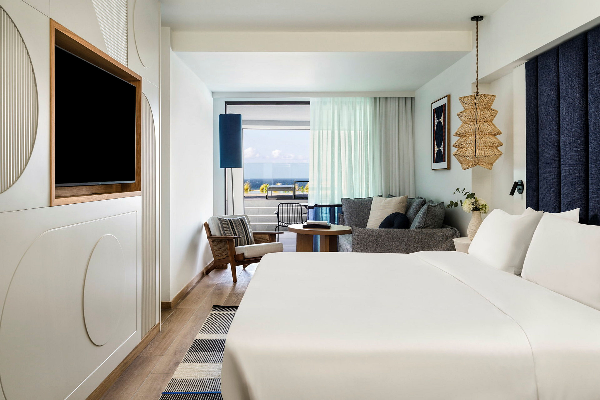 Ett hotellrum med en stor säng, en sittgrupp med glas mot balkong och havsutsikt. (AI-genererad text)