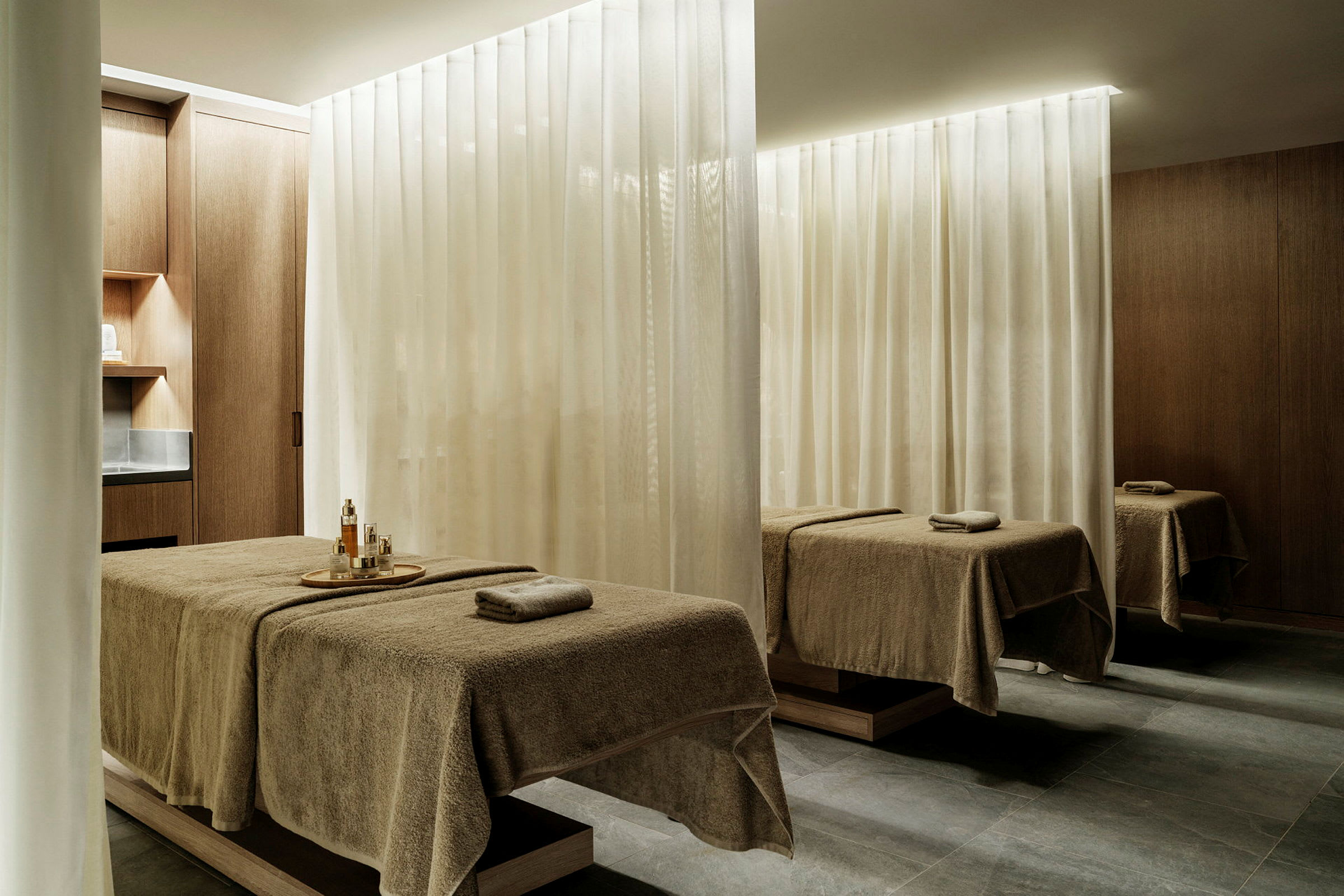 Ett rum med massagebäddar täckta med handdukar, skilt av ljusa gardiner. (AI-genererad text)