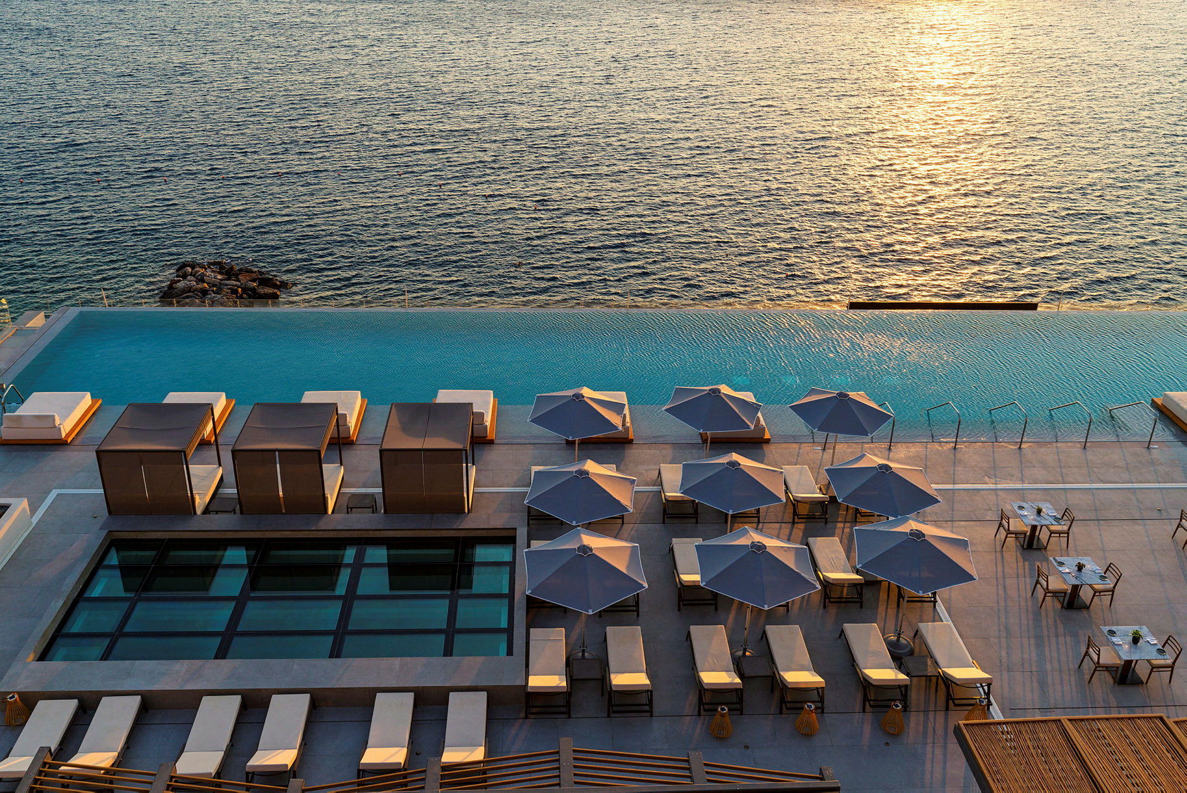 Bild av en pool med solstolar och parasoller vid havet. (AI-genererad text)