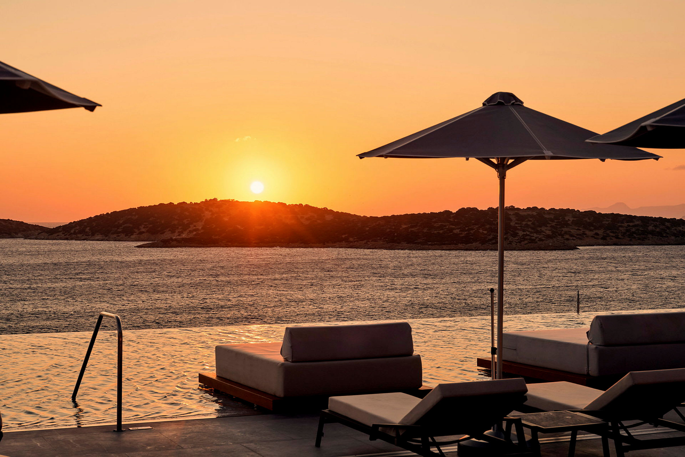 Solnedgång vid havet med solstolar och parasoller vid en infinitypool. (AI-genererad text)