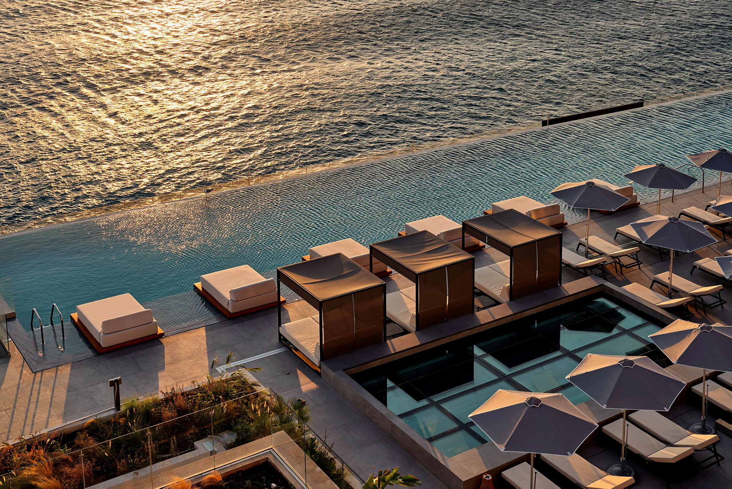 Vy över solstolar och skuggande parasoller vid en infinitypool med havet i bakgrunden. (AI-genererad text)