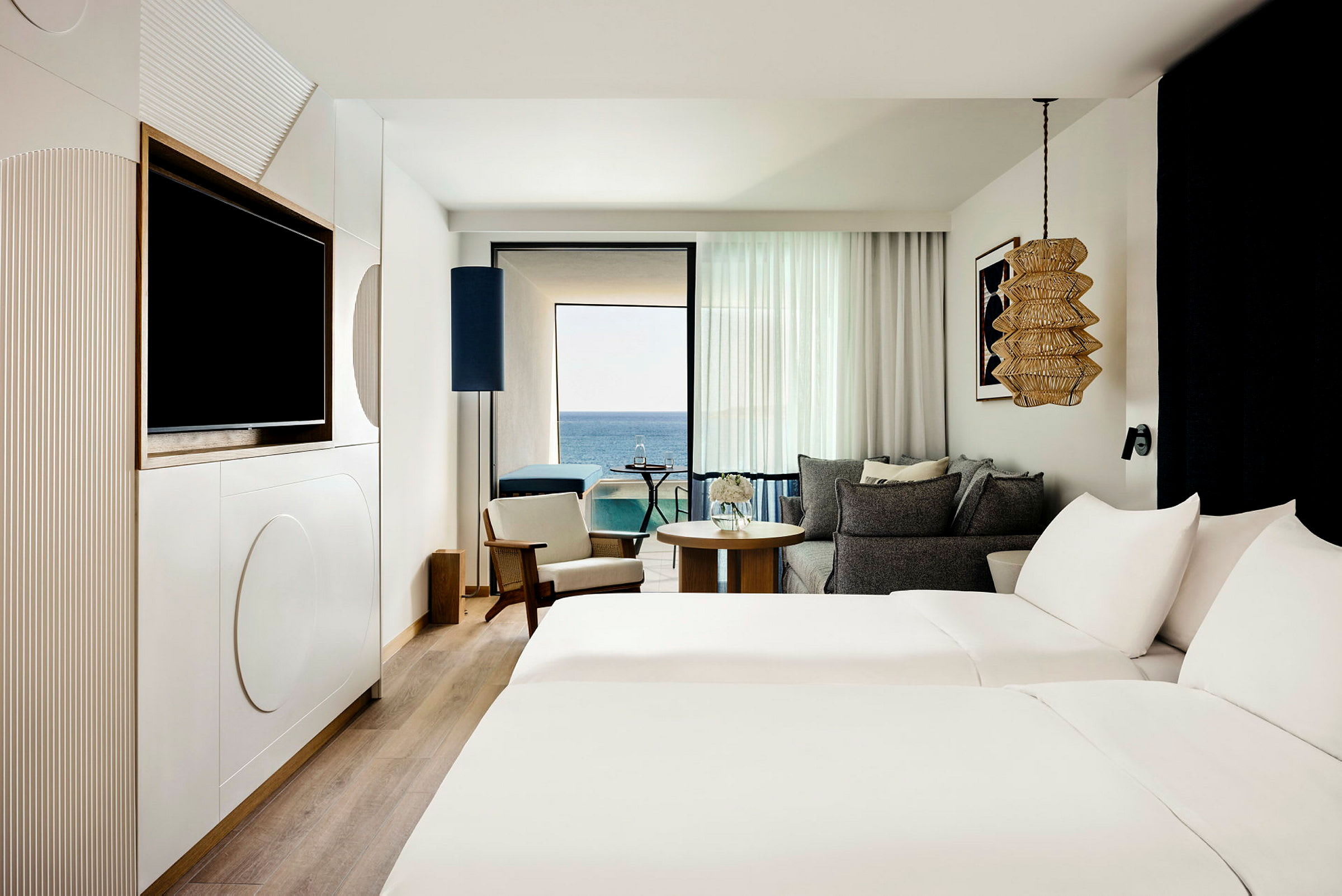 Ett hotellrum med två bäddar, sittmöbler och en balkong med utsikt över havet. (AI-genererad text)