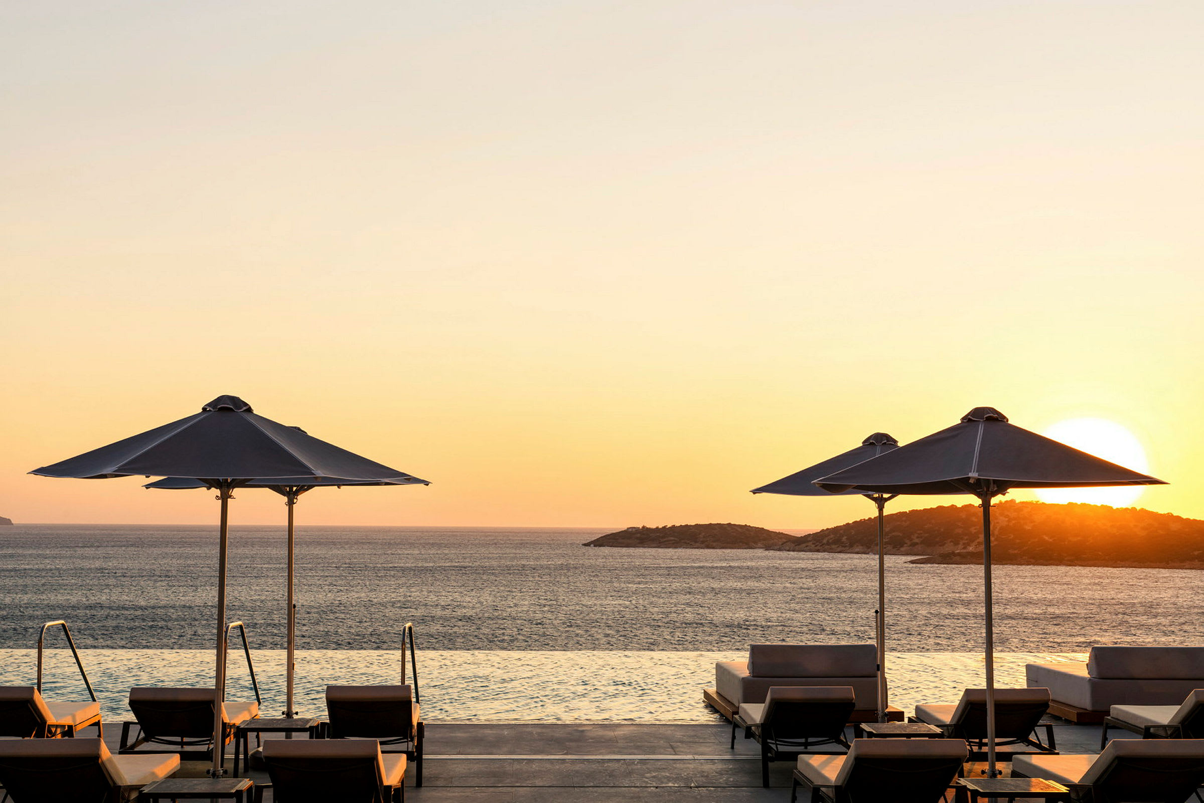 Utsikt över infinitypool med solnedgång och parasoller. (AI-genererad text)