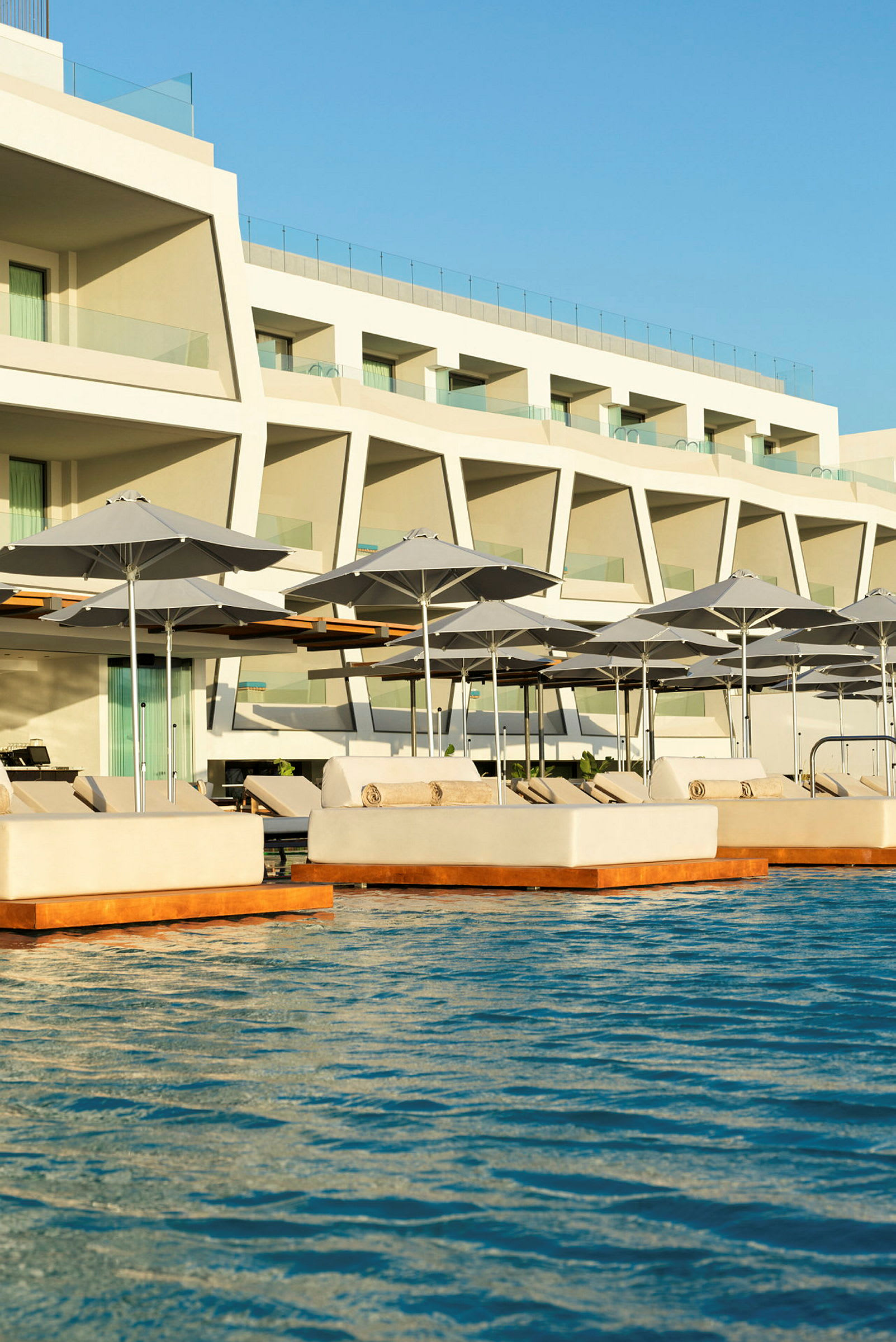Solstolar och parasoller vid en pool framför ett modern hotell. (AI-genererad text)