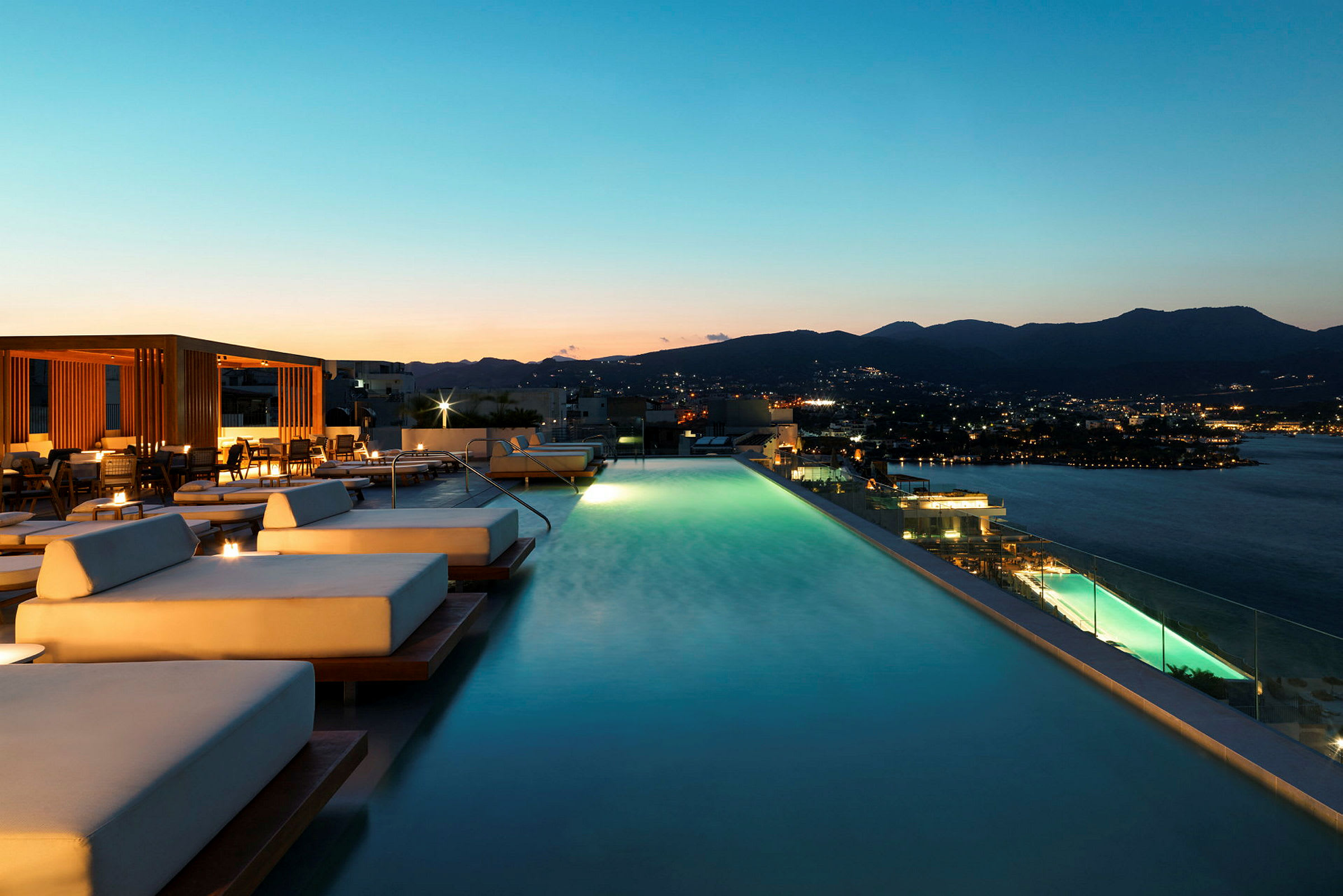 Infinitypool med solstolar vid solnedgång, med utsikt över staden och havet. (AI-genererad text)