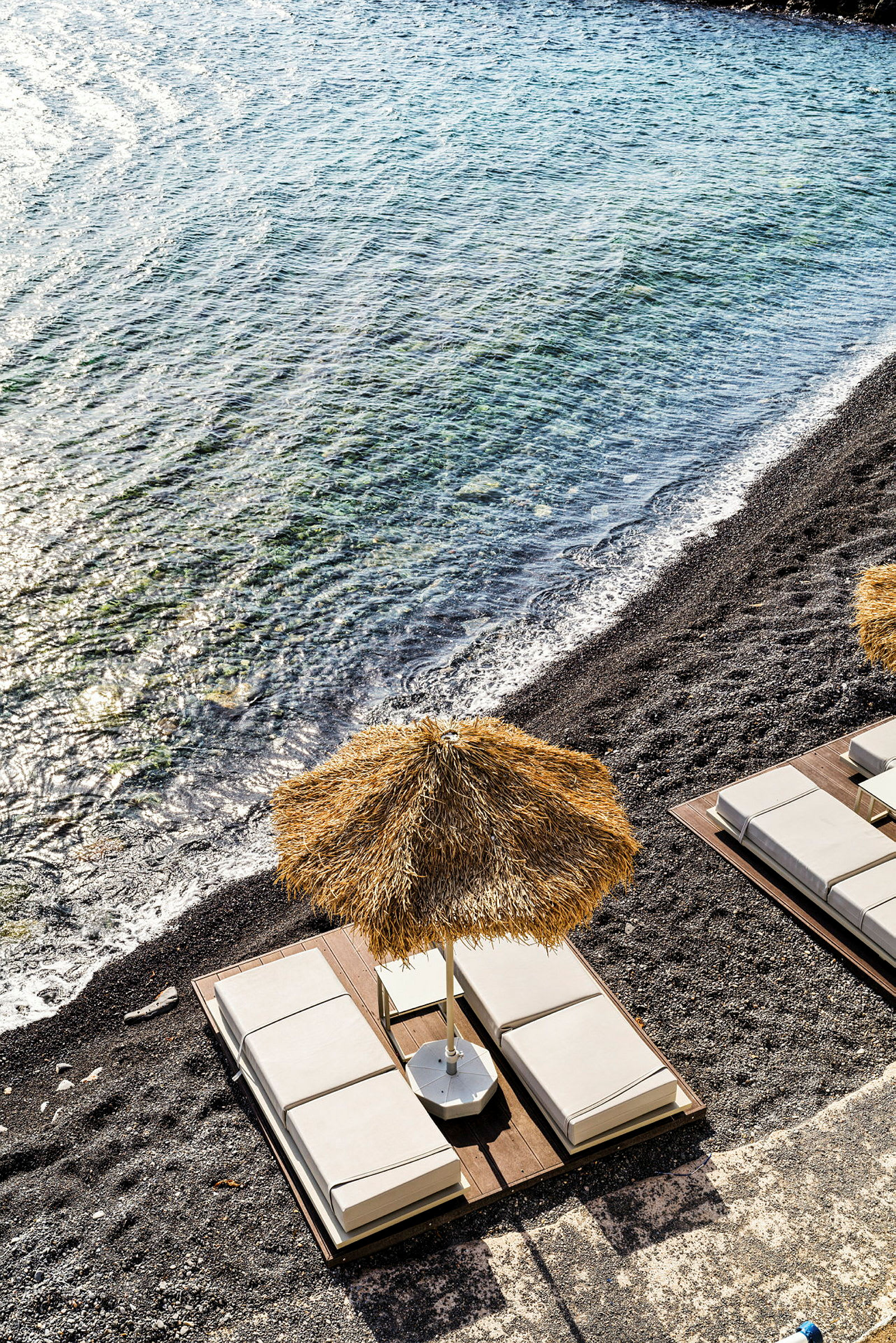 Solstolar med parasoll vid en stenig strand och klart vatten. (AI-genererad text)