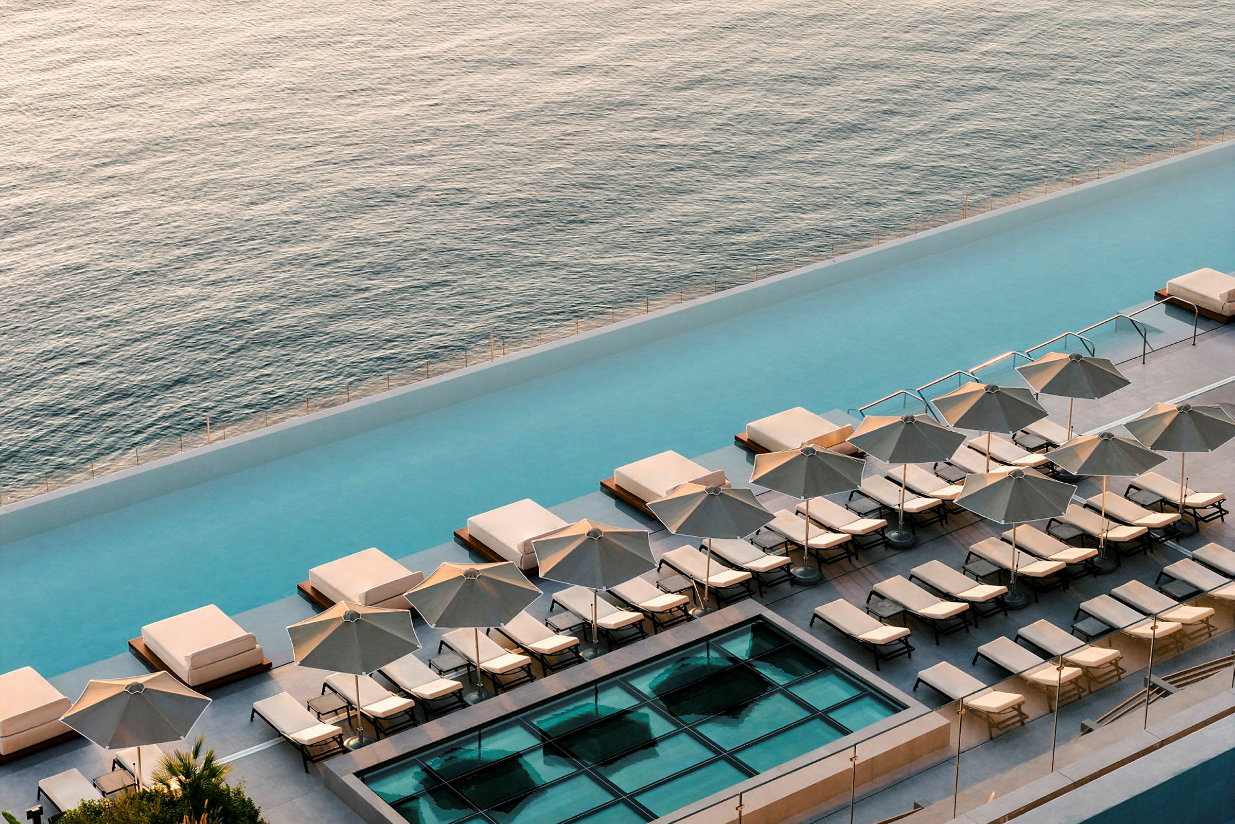 Vy över en pool med solstolar och parasoller vid sidan av havet. (AI-genererad text)