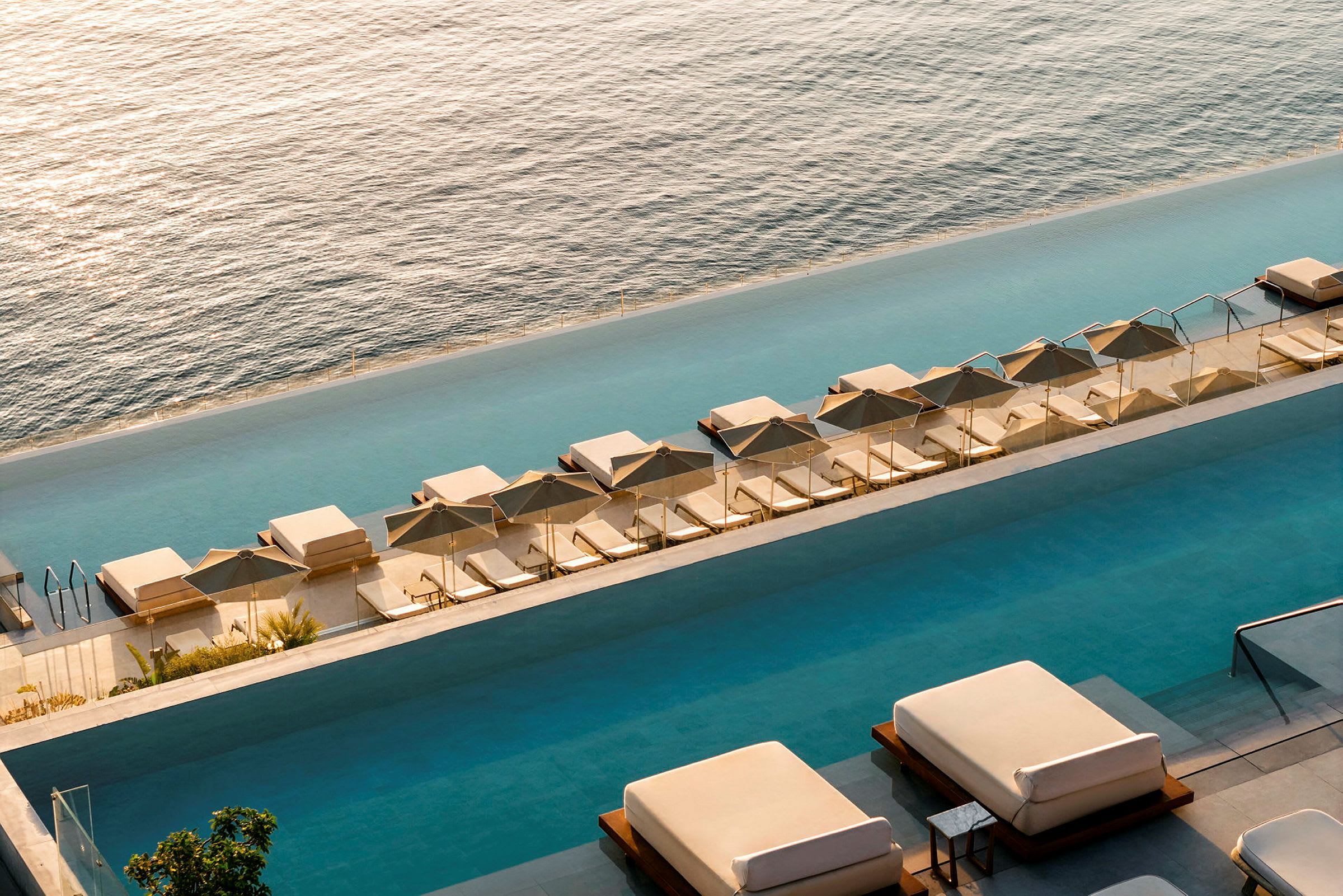 Vy över en infinitypool med solstolar och parasoller, havet i bakgrunden. (AI-genererad text)
