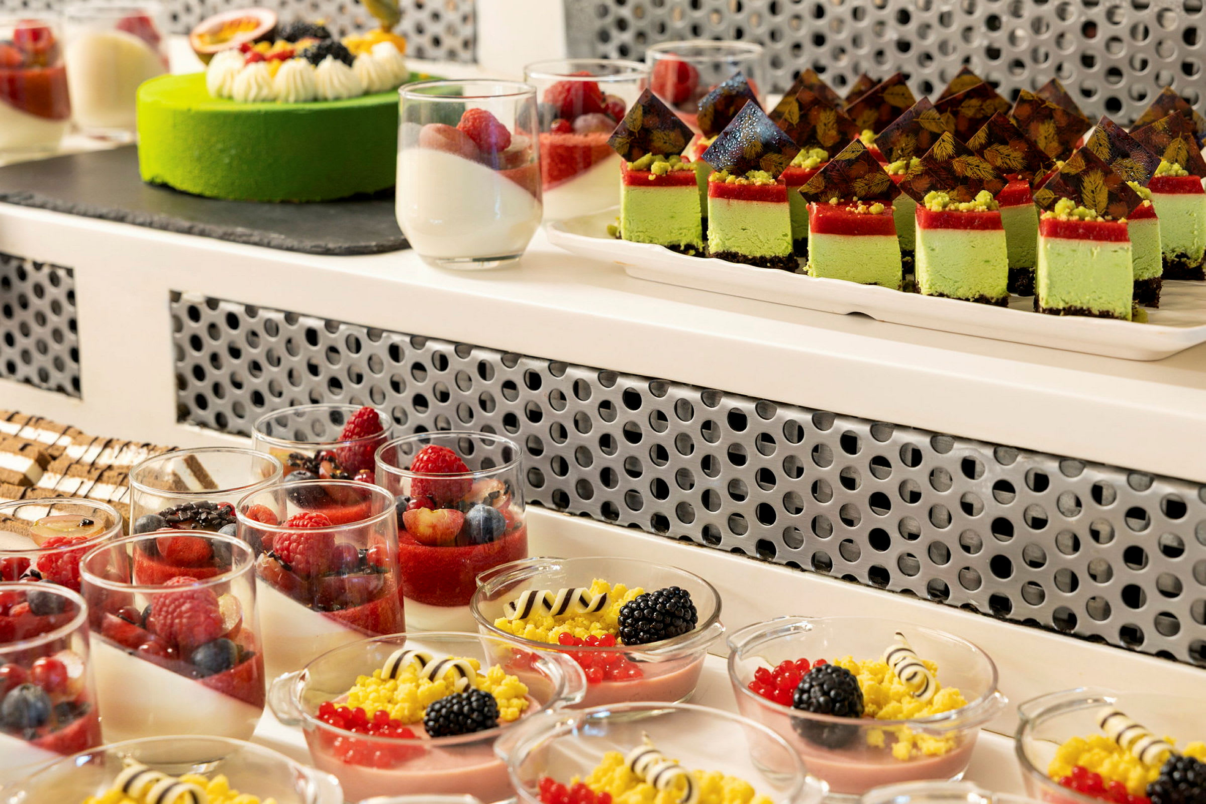 Bild av olika färgglada desserter, inklusive glas med frukt, små tårtbitar och en grön tårta. (AI-genererad text)