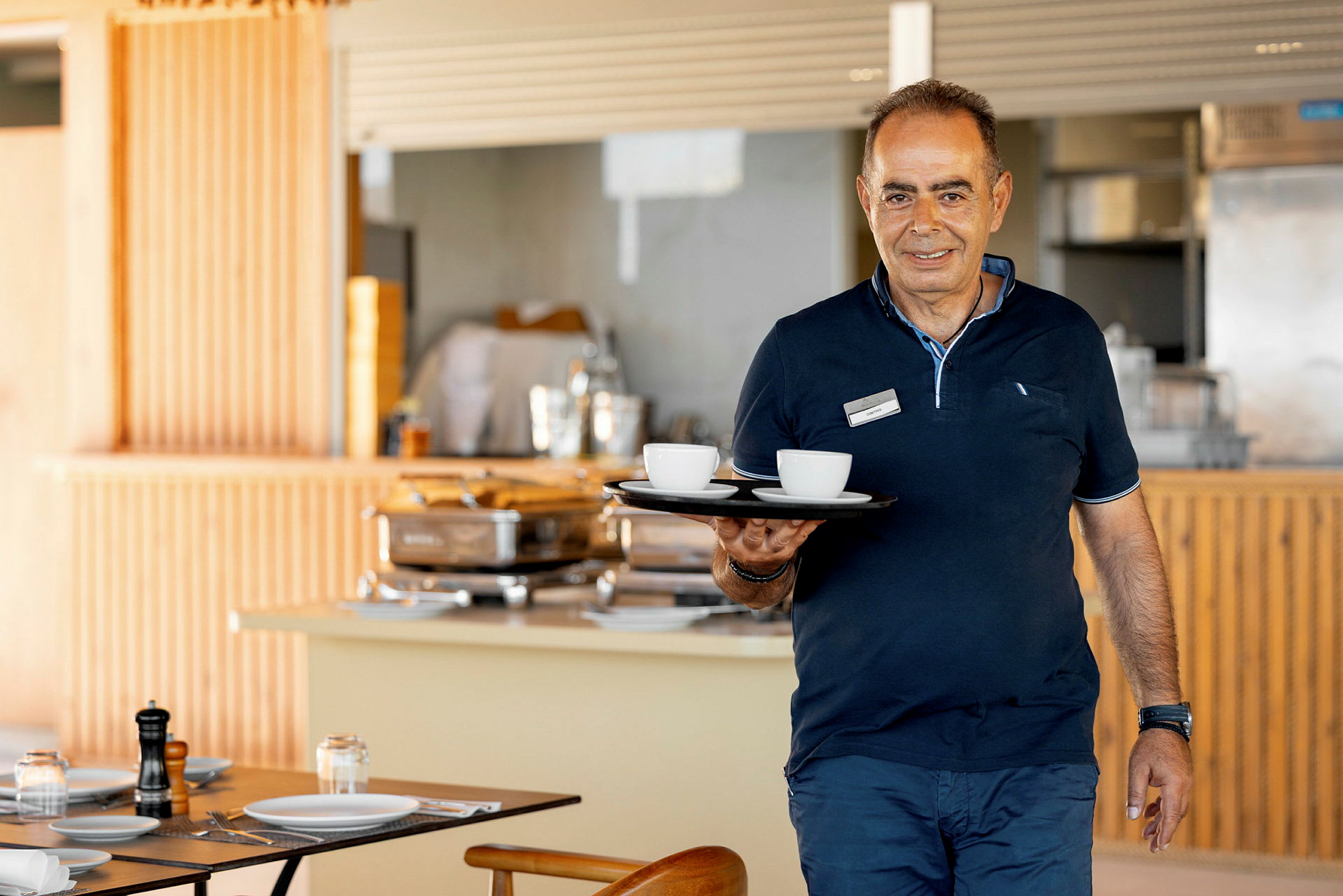 En person håller en bricka med kaffekoppar i en matsal. (AI-genererad text)