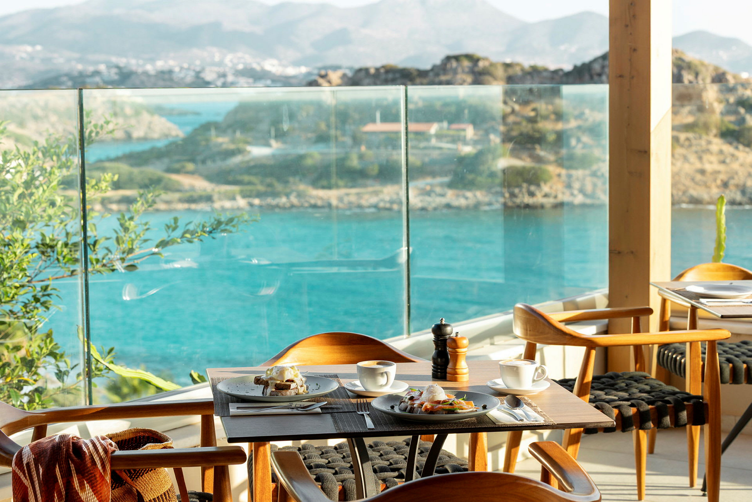 En restaurang med ett bord dukat för frukost, med utsikt över havet och omgivande landskap. (AI-genererad text)