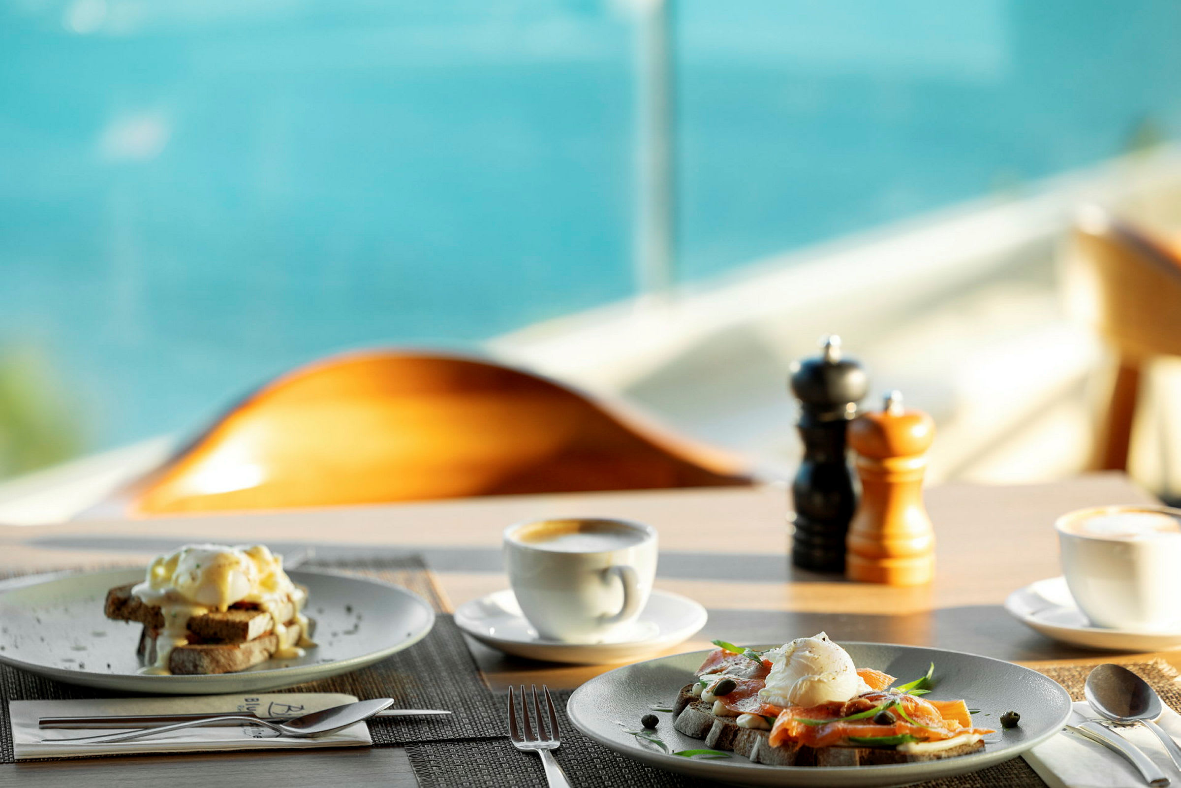 Frukostservering med tallrikar fyllda med äggrätter, kaffe och havsutsikt i bakgrunden. (AI-genererad text)