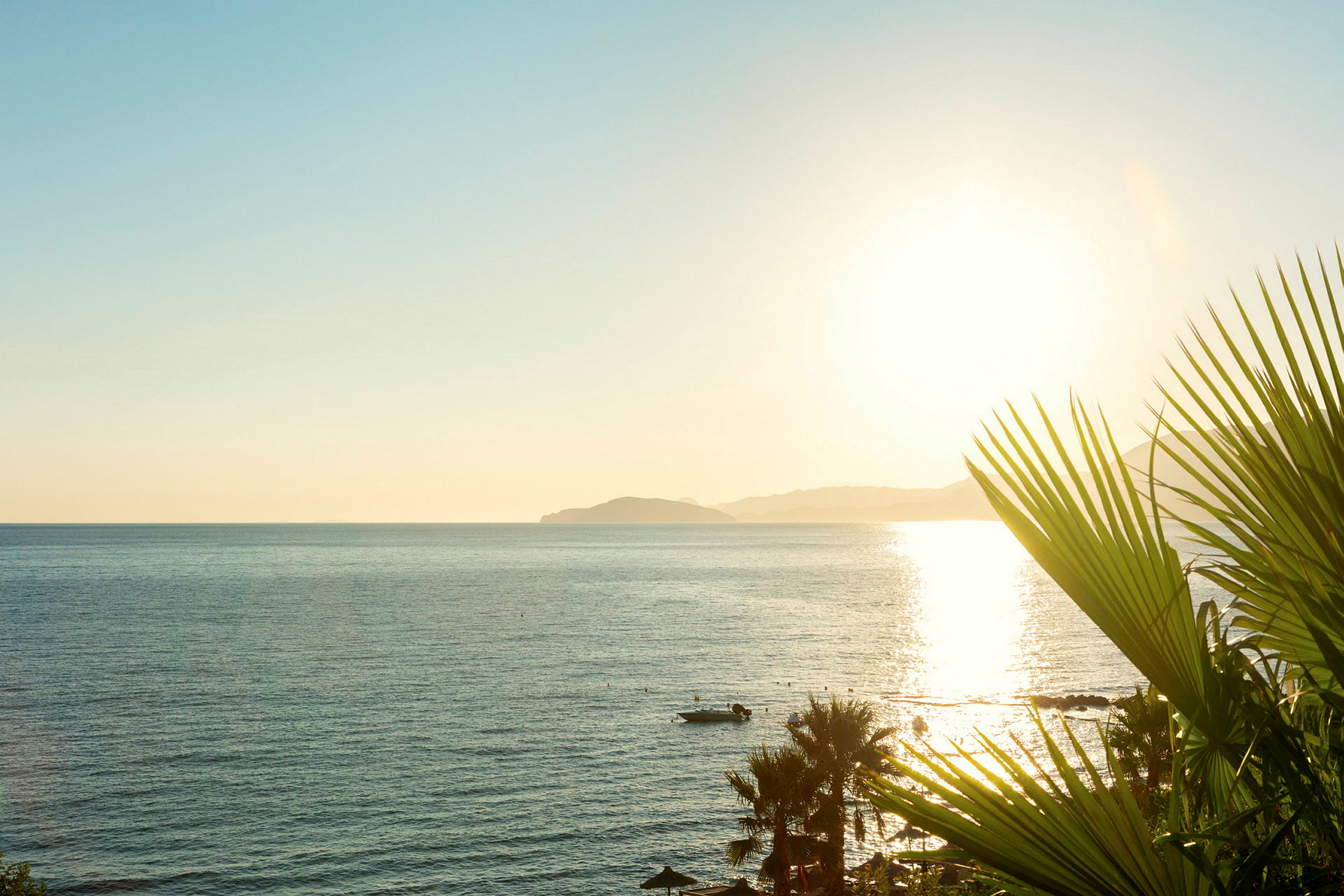 Utsikt över havet med solnedgång, palmer och en liten båt. (AI-genererad text)