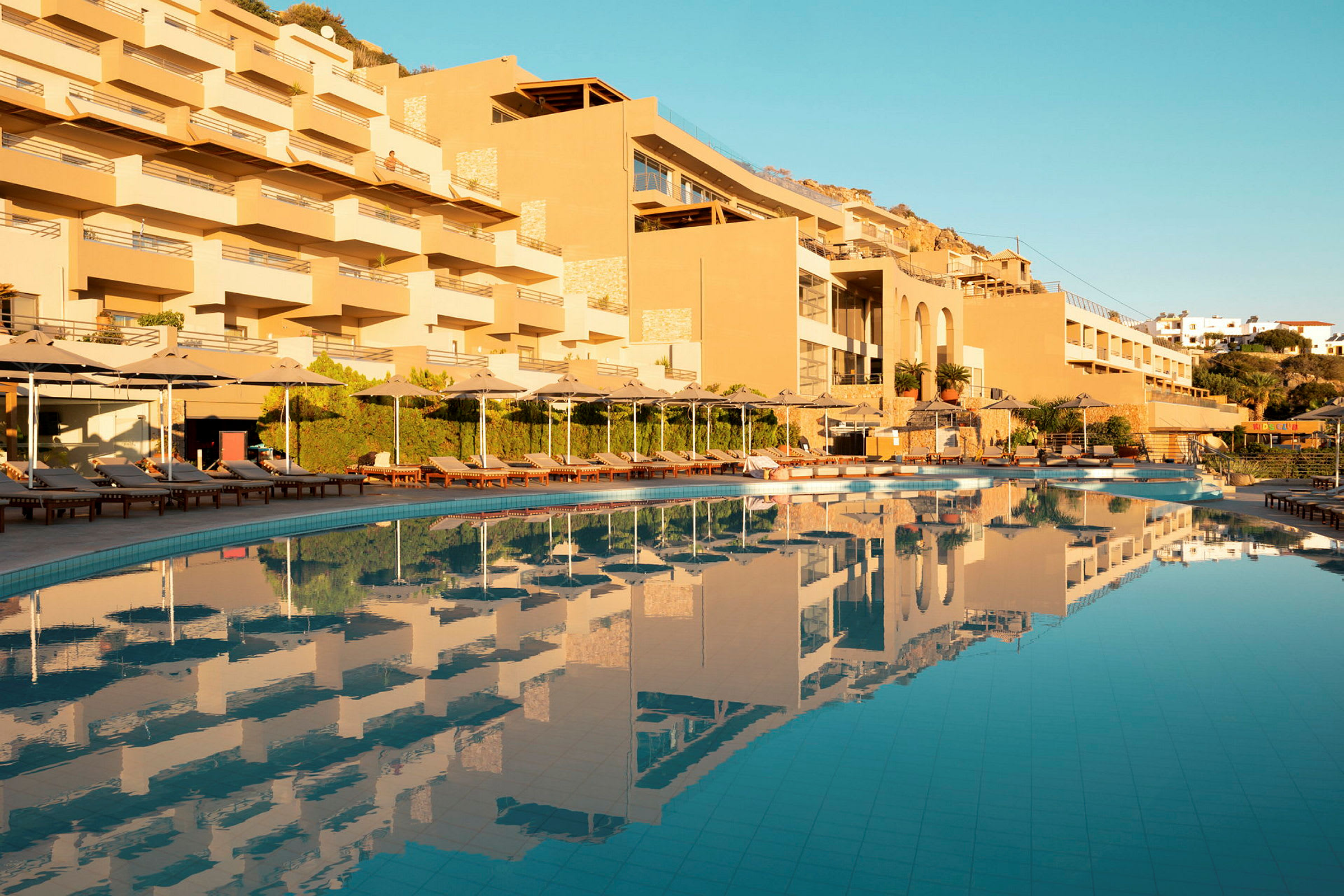 Hotellets byggnad med pool och solstolar vid solnedgången. (AI-genererad text)
