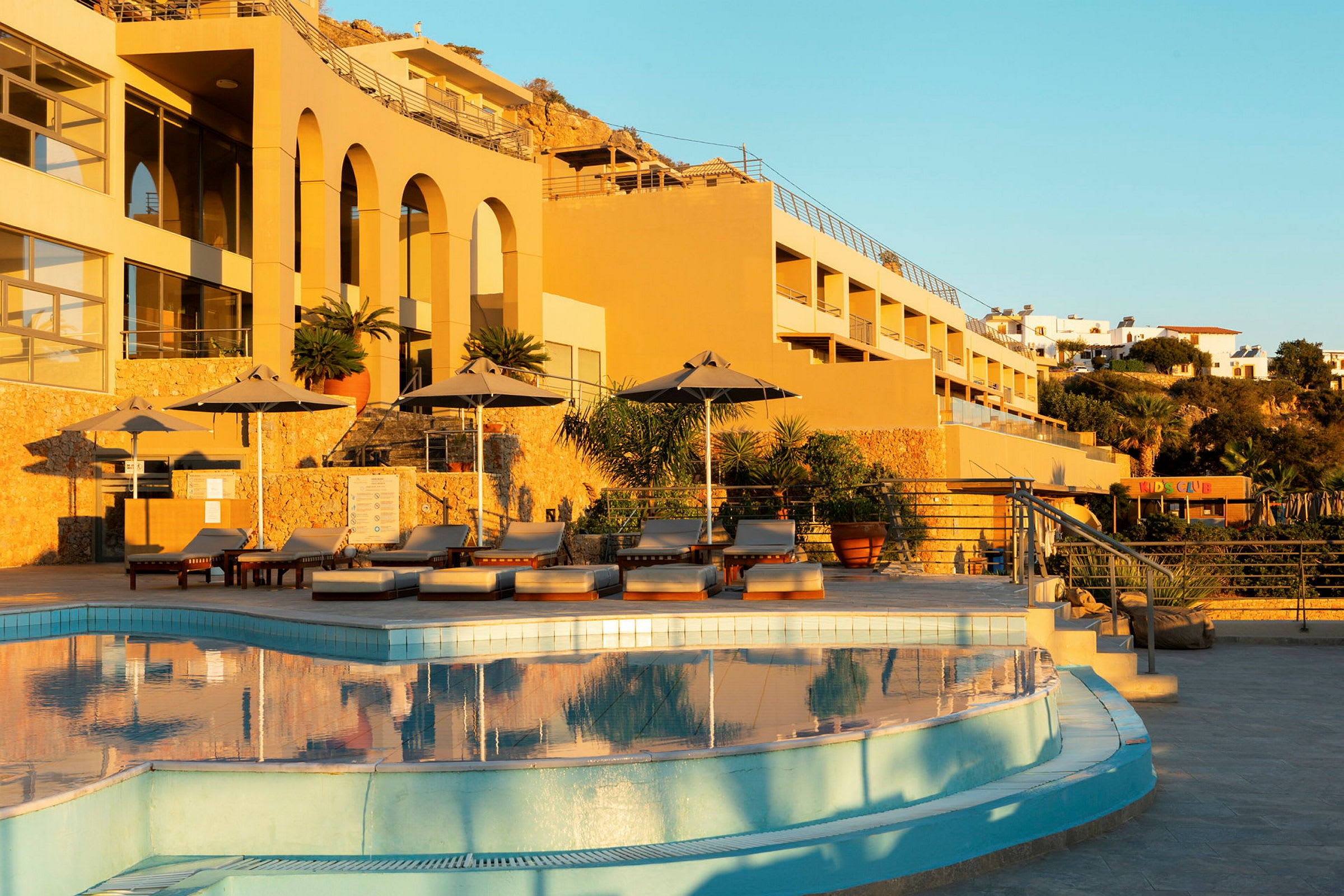 Solupplyst hotellbyggnad med en pool och solstolar i förgrunden. (AI-genererad text)