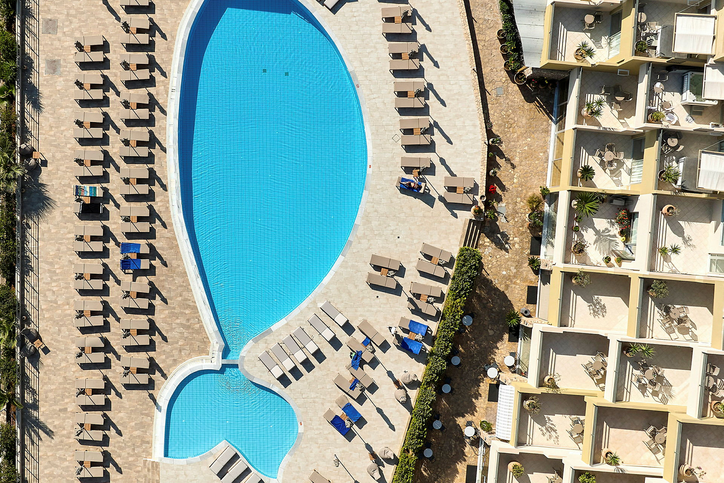Flygbild över en pool med solstolar bredvid och omgivande lägenheter. (AI-genererad text)
