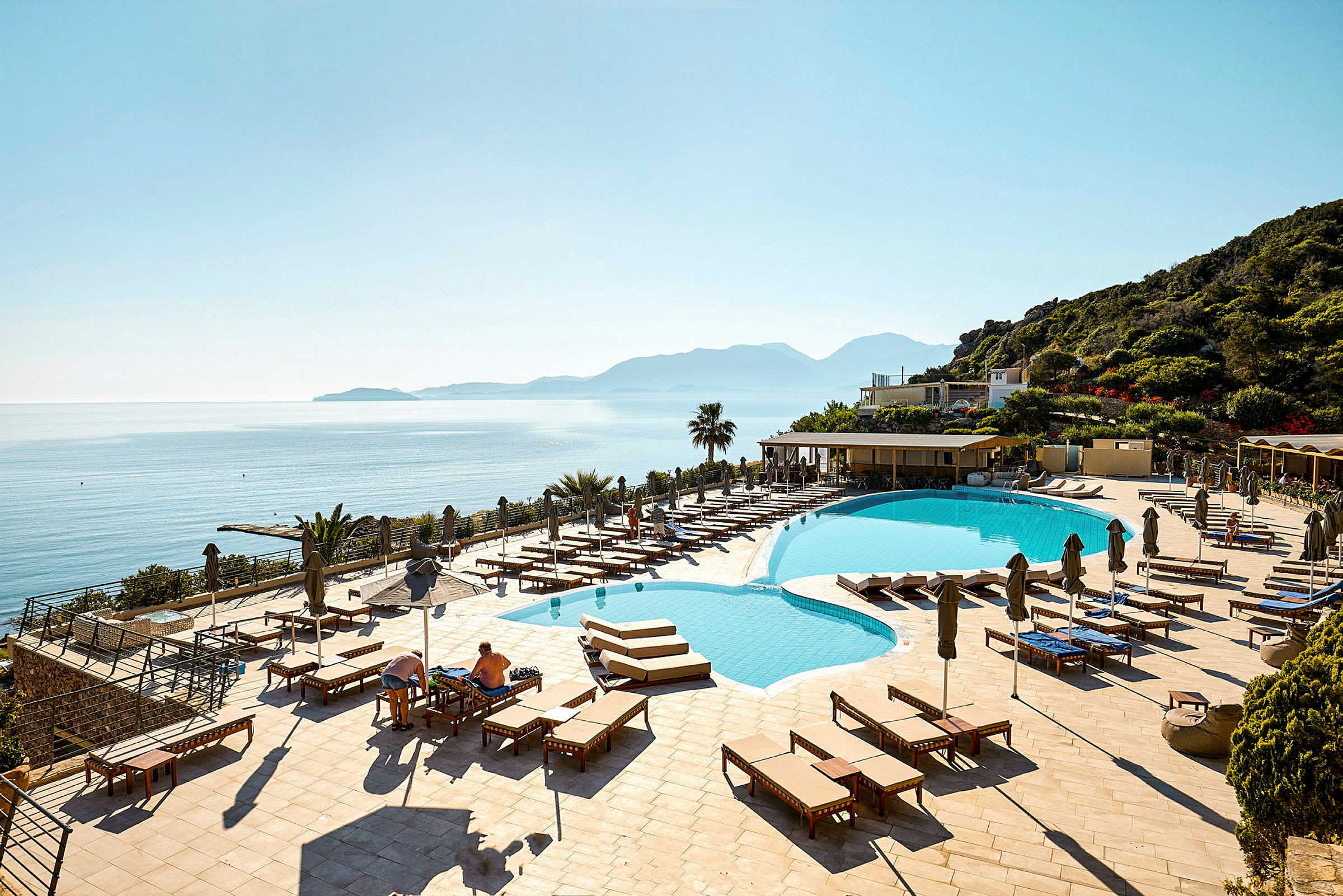 Hotellpool med solstolar och utsikt över havet och berg. (AI-genererad text)