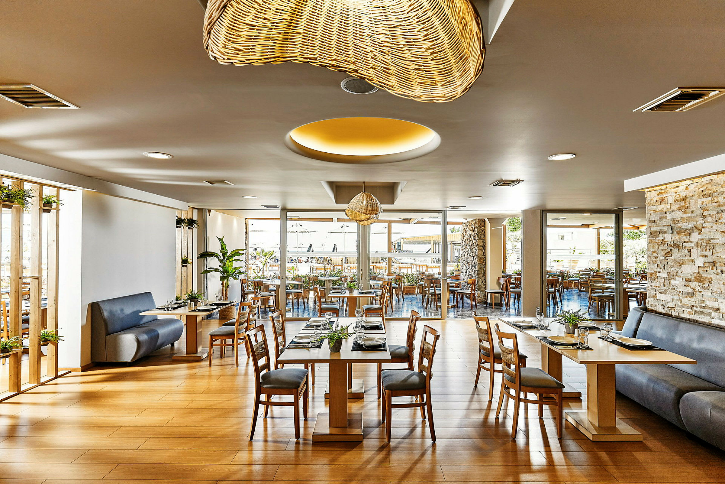 En modern restaurang med träbord och stolar, dekorativ belysning och stora fönster mot en uteservering. (AI-genererad text)