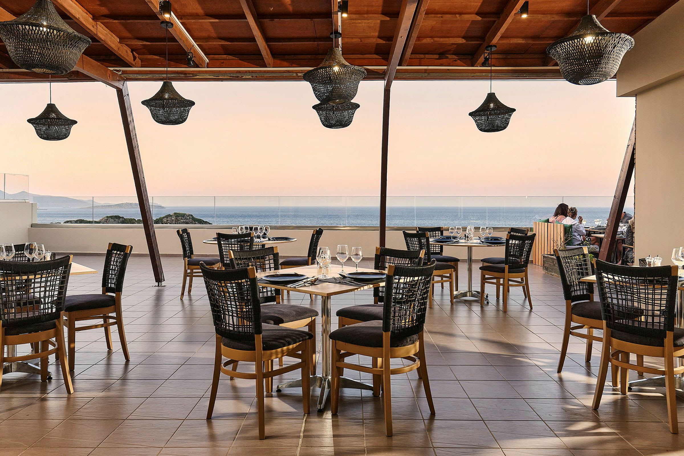 En restaurang med bord och stolar på en terrass med utsikt över havet. (AI-genererad text)