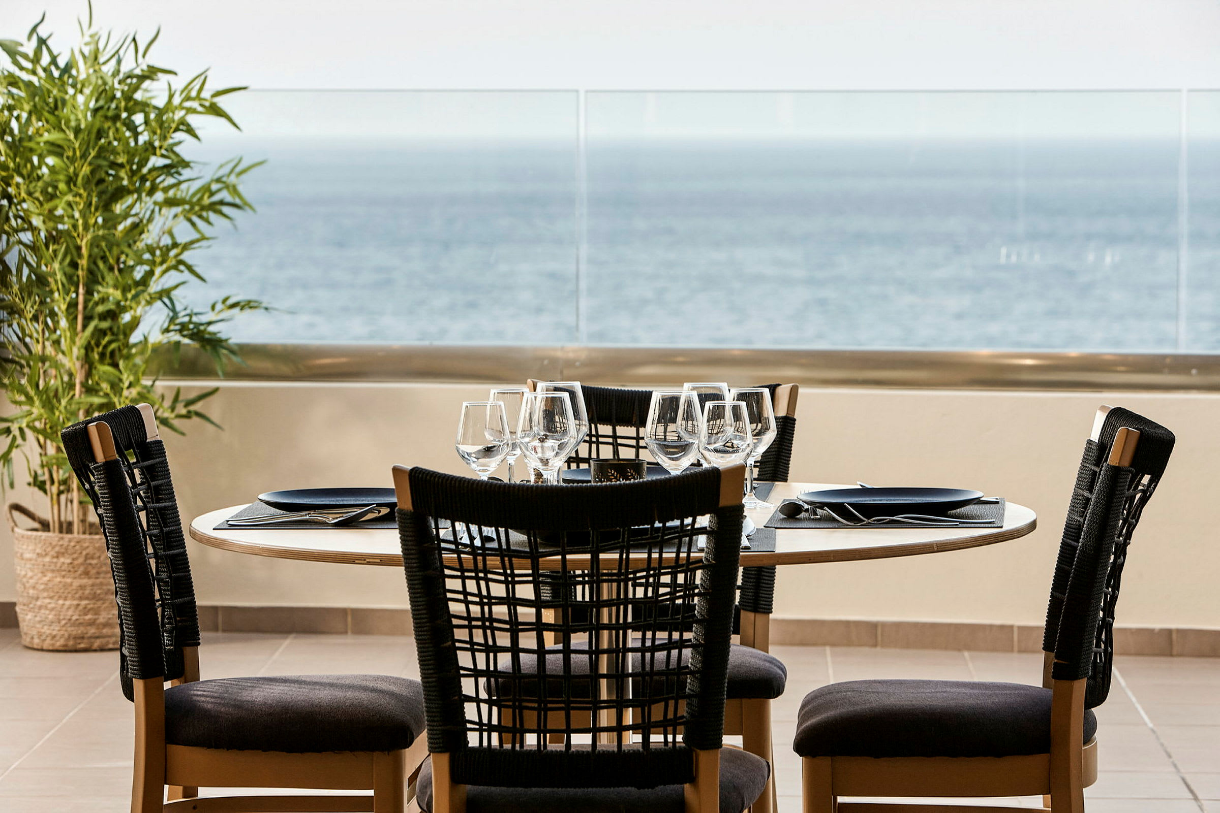 Ett dukat bord med stolar vid en balkong med utsikt över havet. (AI-genererad text)