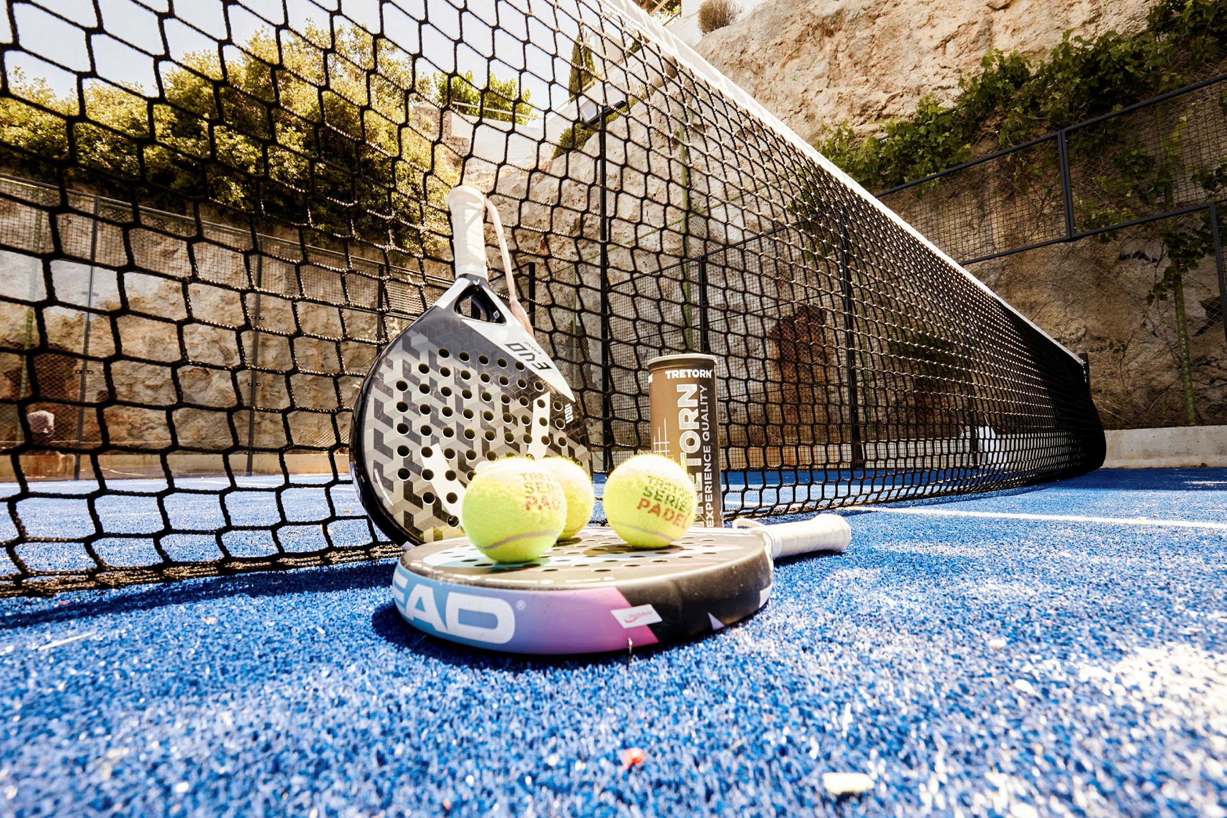 En padelbana med en racket och bollar som ligger på den blå mattan nära nätet. (AI-genererad text)
