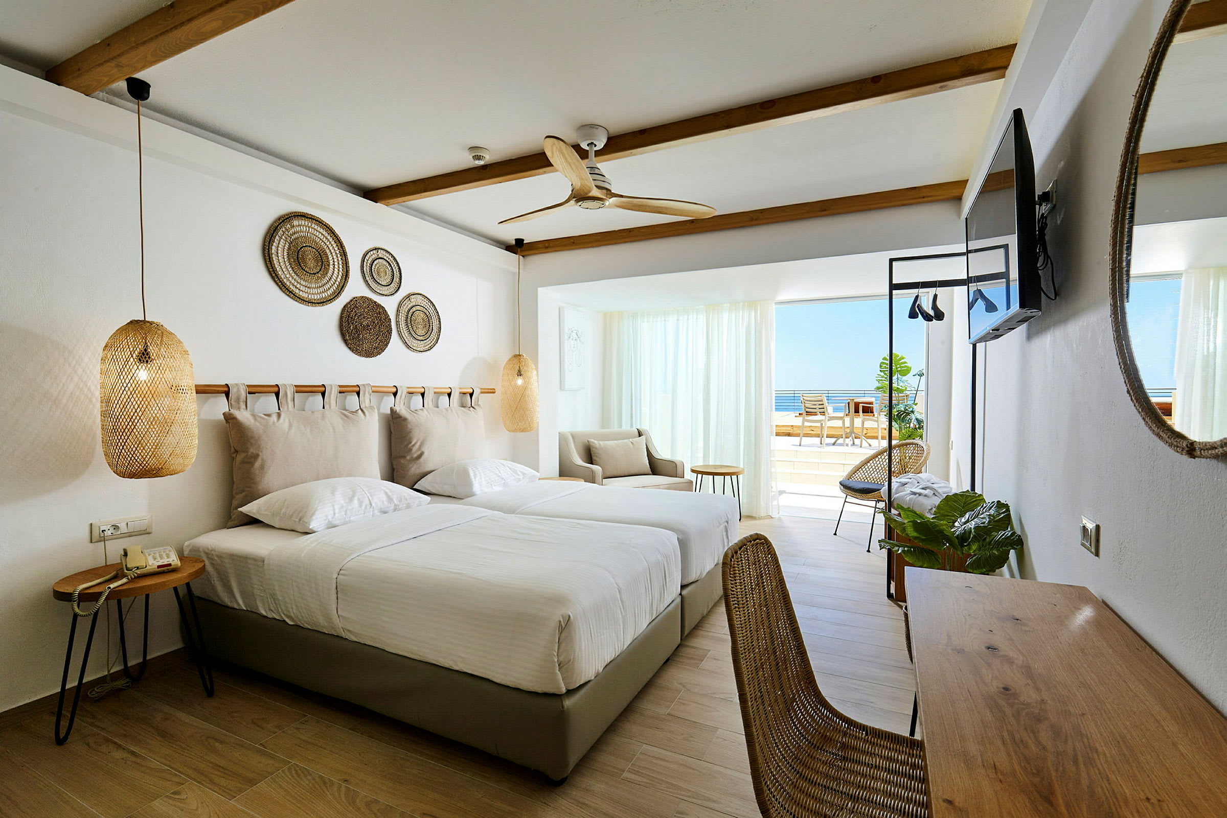 Hotellrum med två enkelsängar, sittgrupp och balkong med havsutsikt. (AI-genererad text)