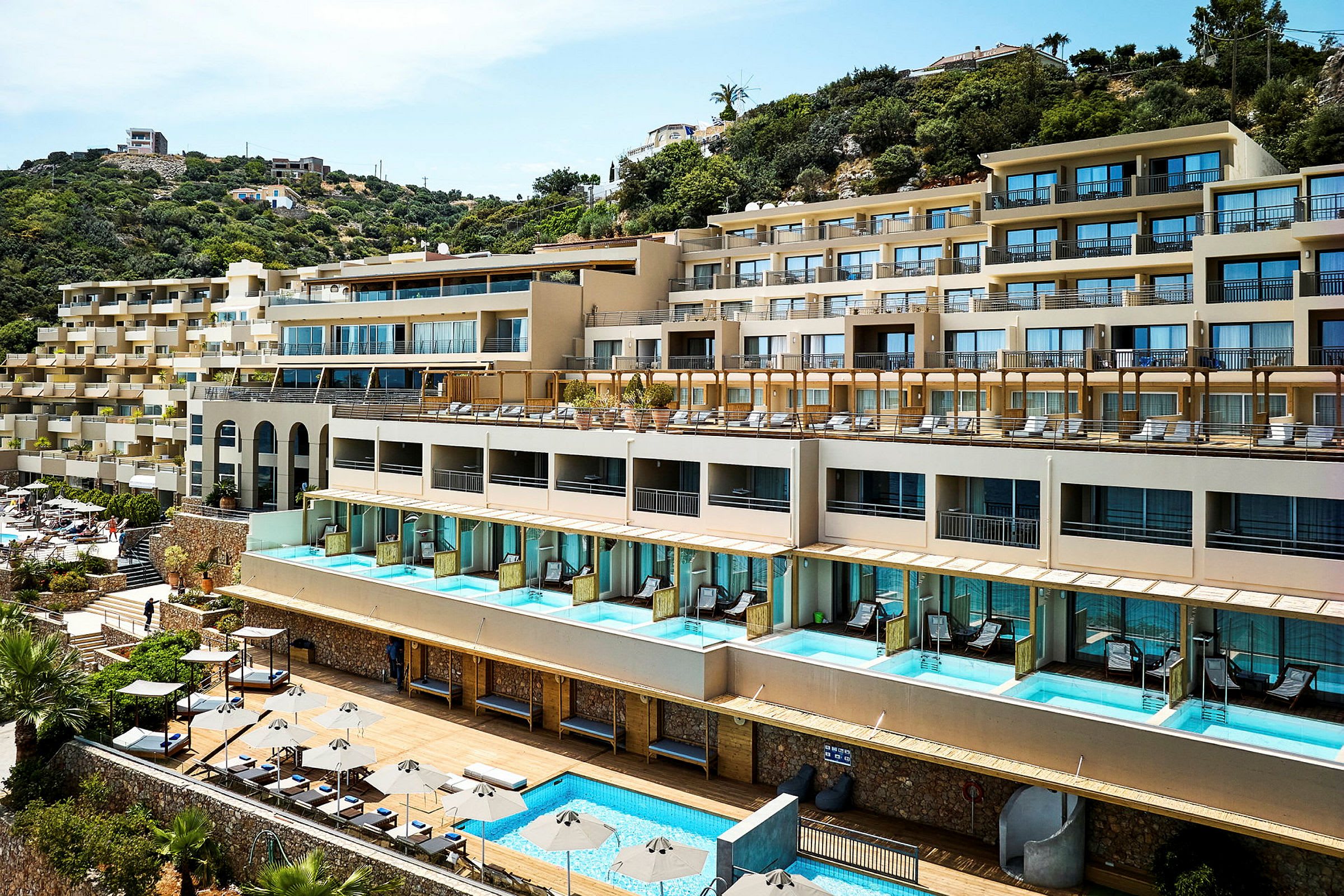 Hotellkomplex med pooler och solstolar vid en sluttning. (AI-genererad text)