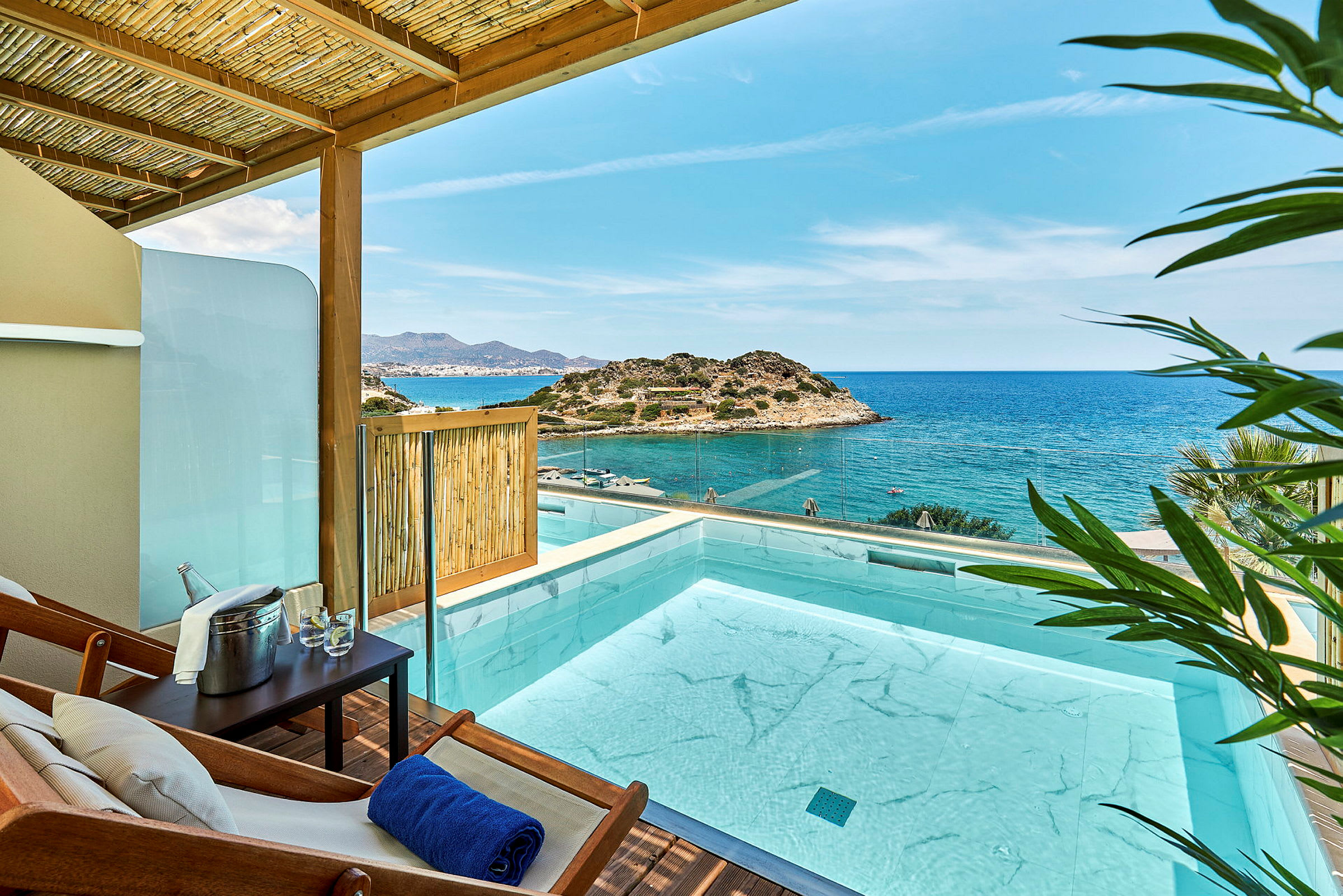 Utsikt över en pool på en terrass med hav och klippiga kullar i bakgrunden. (AI-genererad text)